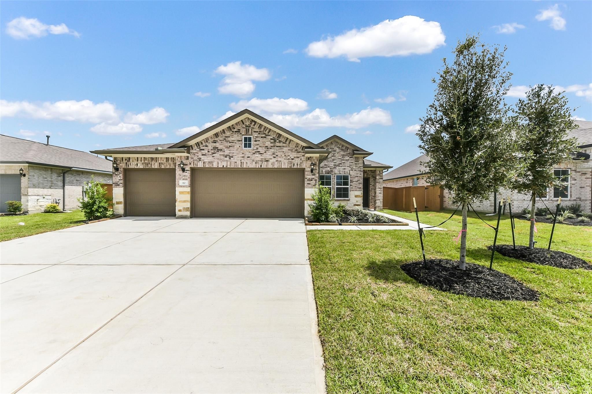Modern brick single-story home with 3-car garage, concrete driveway, and landscaped yard in River Ranch Meadows, Dayton, Texas