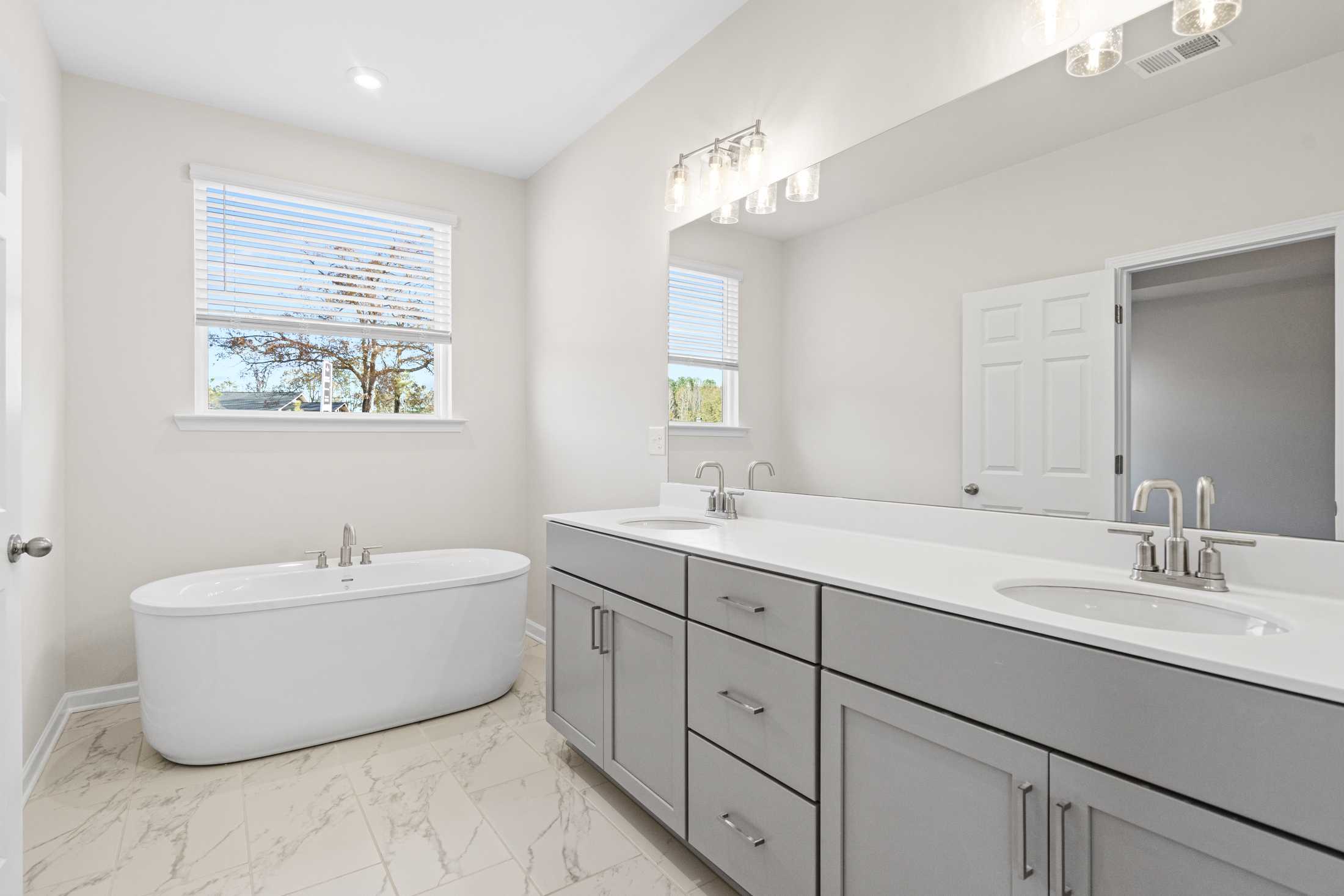 Spacious master bath in The Glenwood A featuring freestanding tub, double gray vanity, and window light