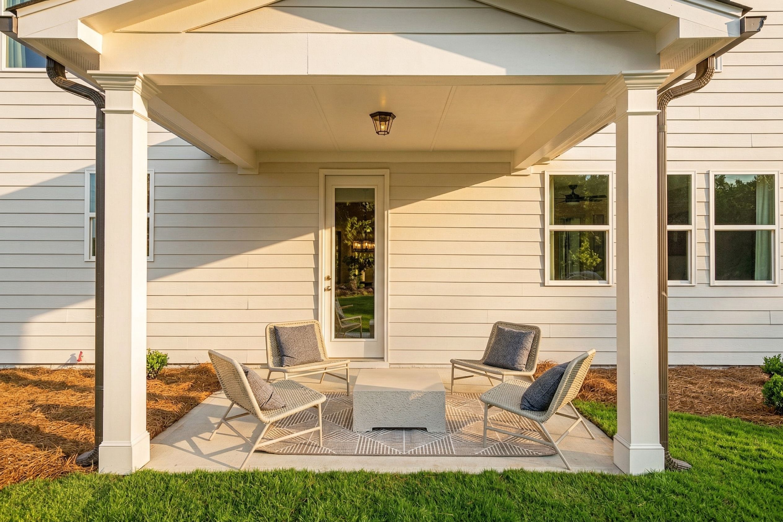 Covered patio at Wehunt Meadows in Hoschton Georgia with white columns, lounge chairs, coffee table, and glass door