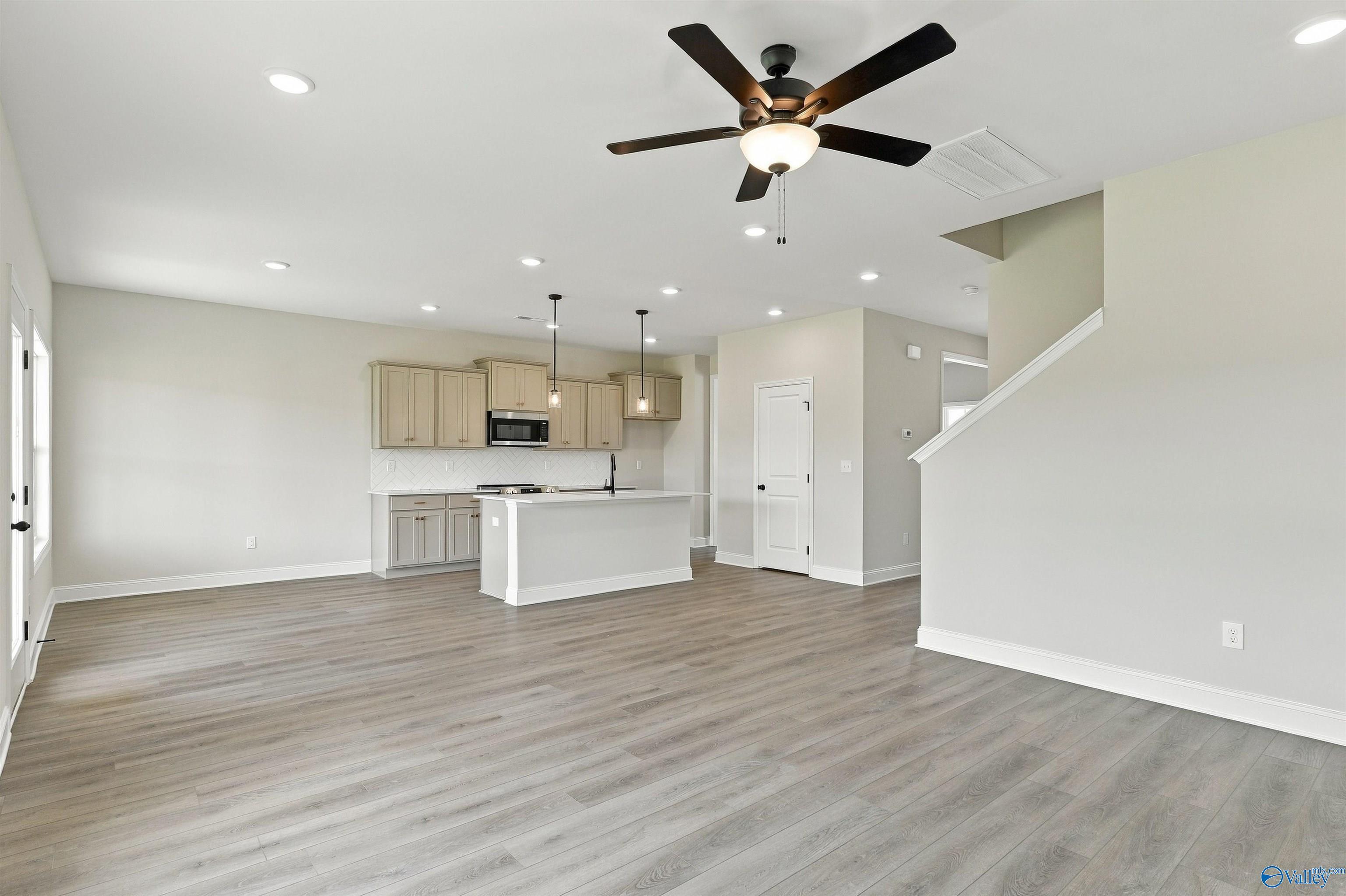 Open-concept great room with luxury vinyl plank flooring, kitchen island, and ceiling fan in Davidson Homes The Shelby A, Athens, AL