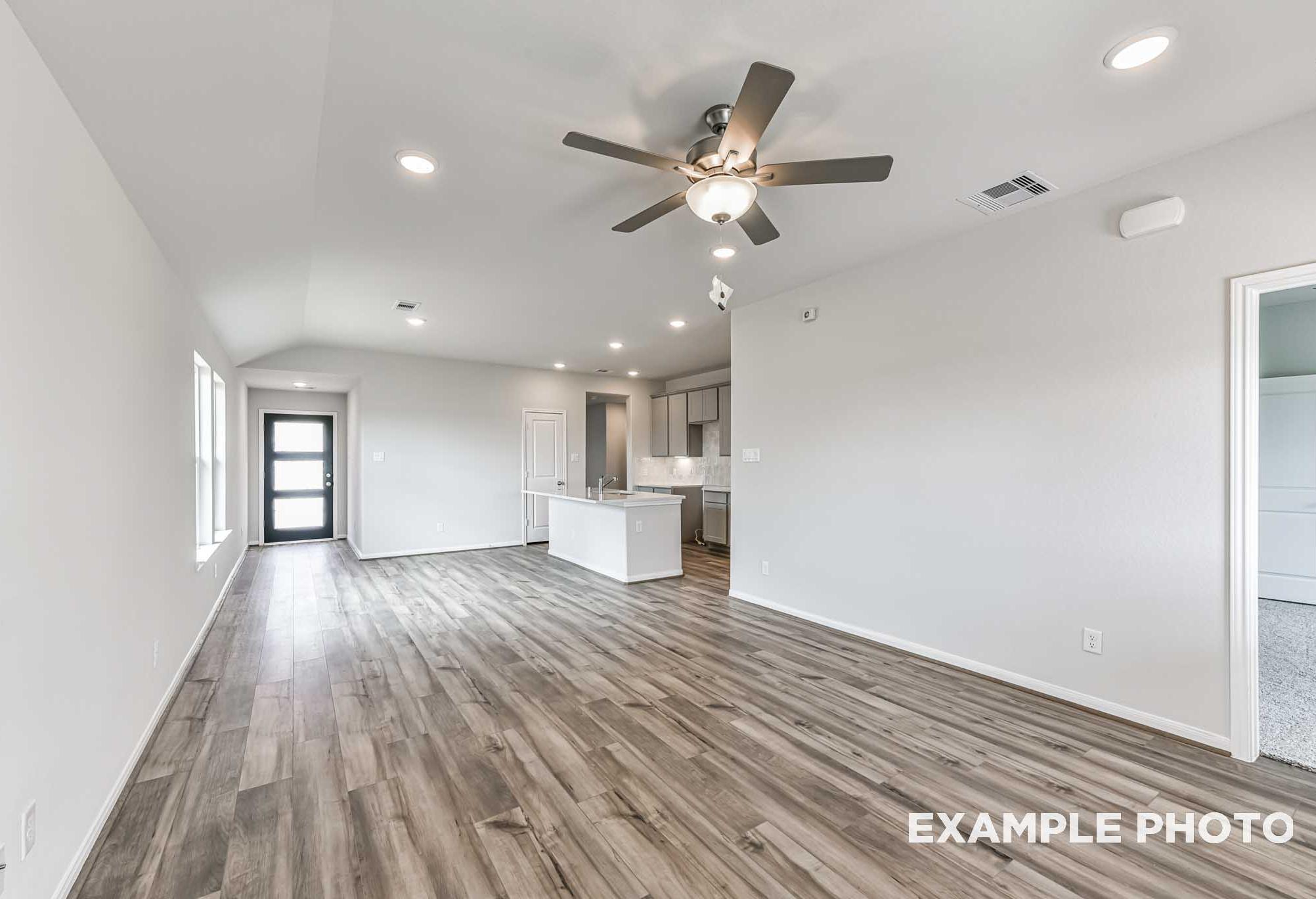 Spacious open-concept living room and kitchen in The Costa A by Davidson Homes, with hardwood floors, white cabinets and ceiling fans