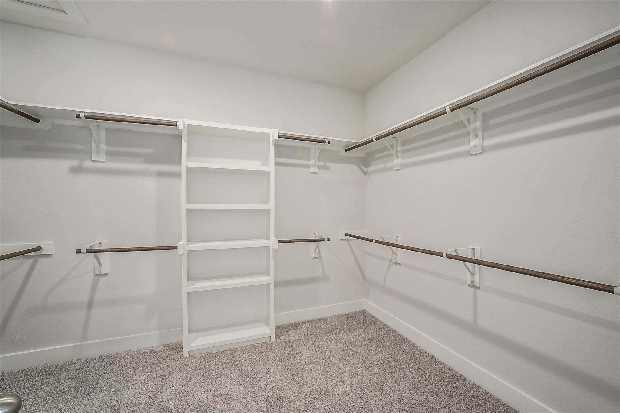 Spacious walk-in closet with wooden shelves, hanging rods, and carpeted floor in Davidson Homes The Philip B, Rosharon, Texas
