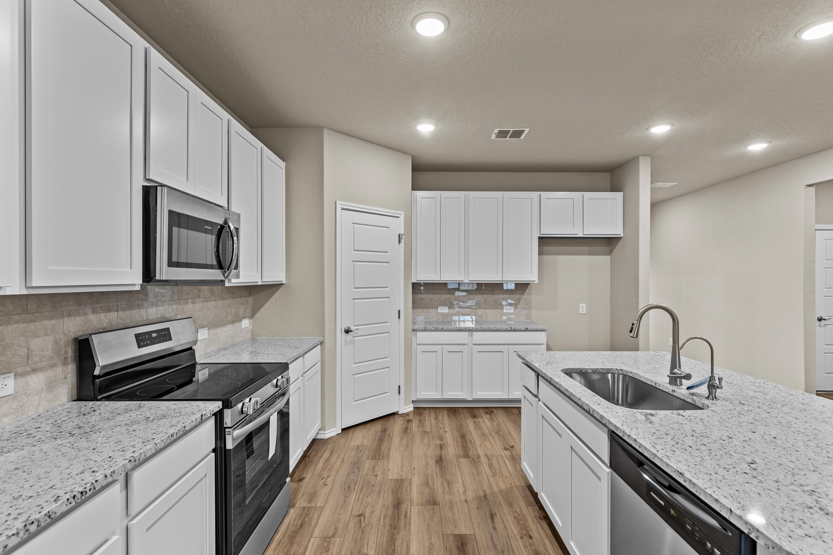 Modern white kitchen with granite island, stainless steel appliances, subway tile backsplash in Davidson Homes The Douglas F, San Antonio