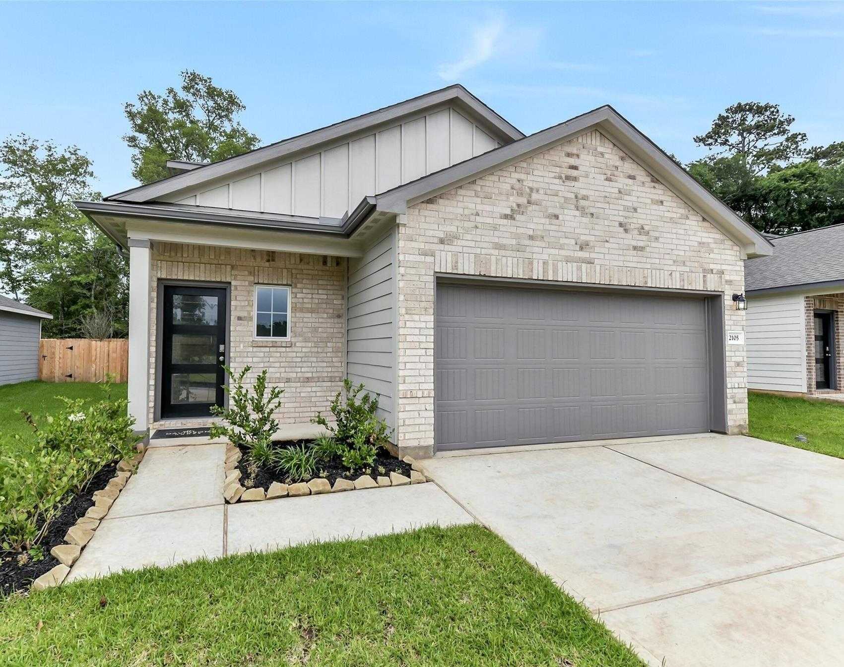 Modern 2-story light brick home with gray siding, 2-car garage, and front landscaping in Caney Creek Place, Conroe, Texas