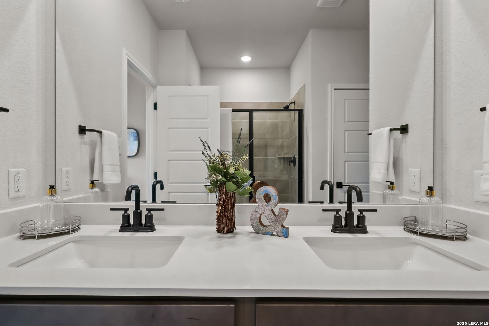 Modern master bathroom double vanity with chrome faucets, mirrors, towels, flowers in Davidson Homes The Daphne H, Seguin, TX
