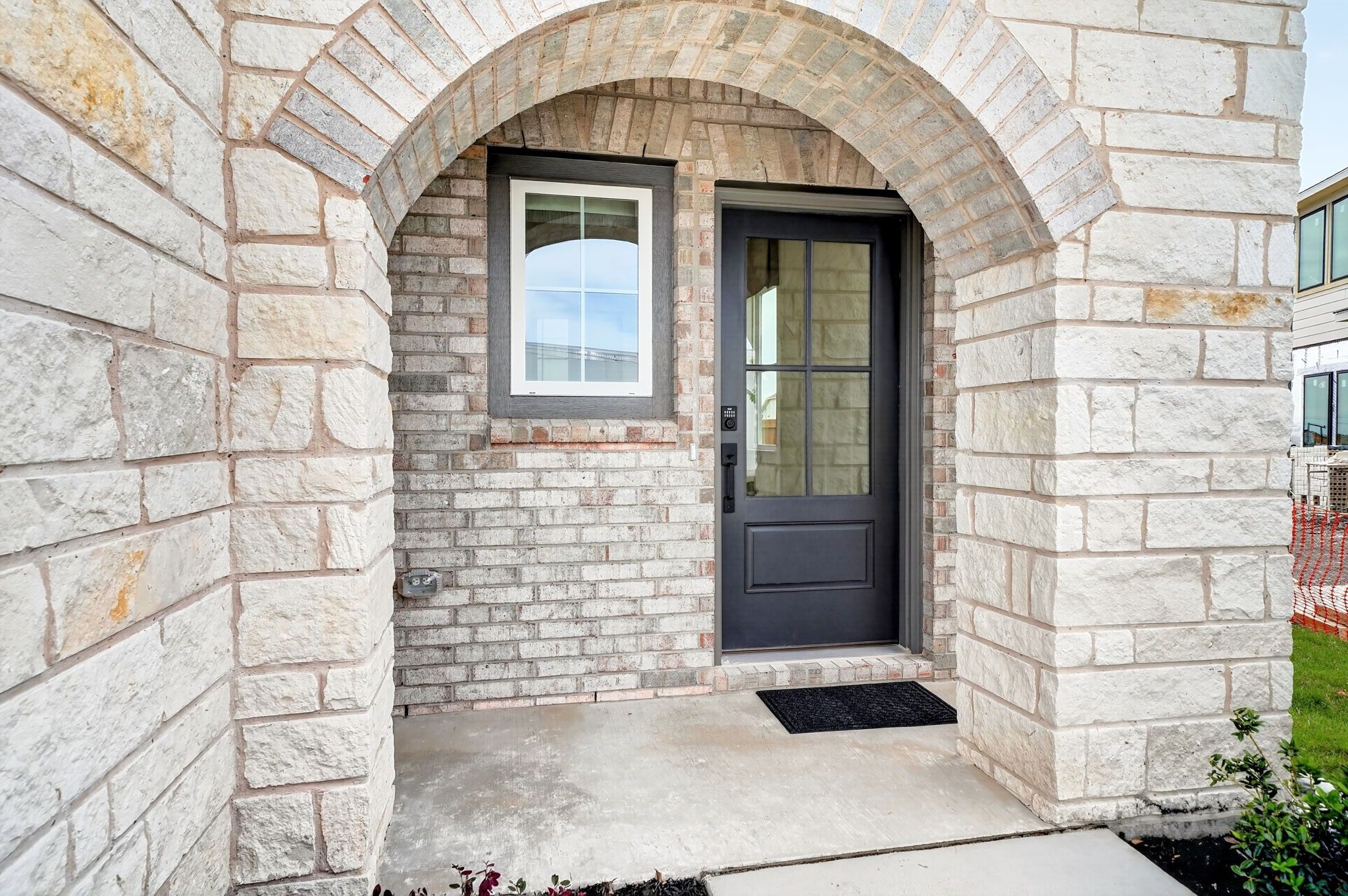 Arched stone entryway with dark glass front door at The Sabine J floor plan by Davidson Homes in Heartland, Texas.