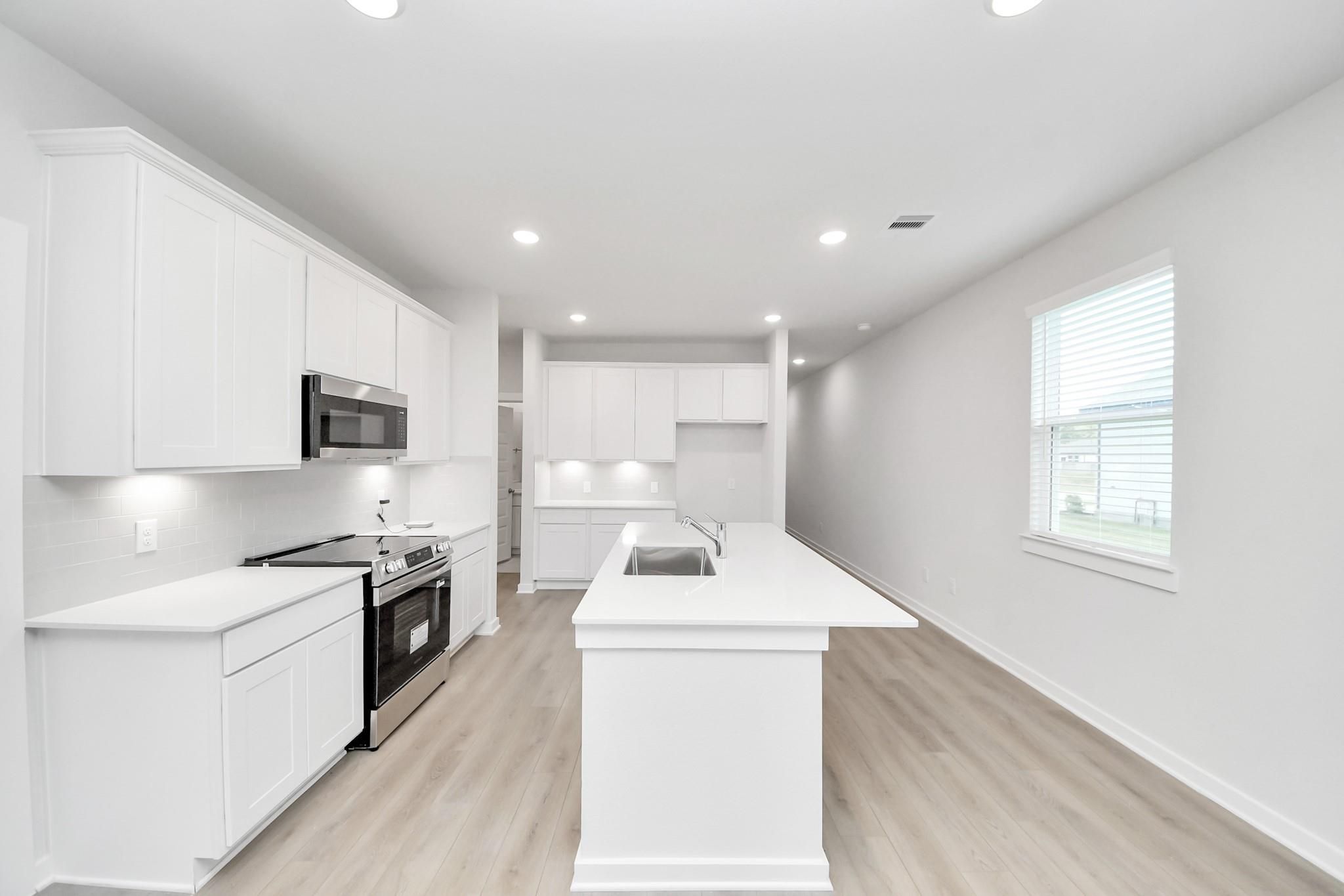 Modern white kitchen with island, quartz countertops, and stainless appliances in The Frio F plan, Liberty Estates, Texas.