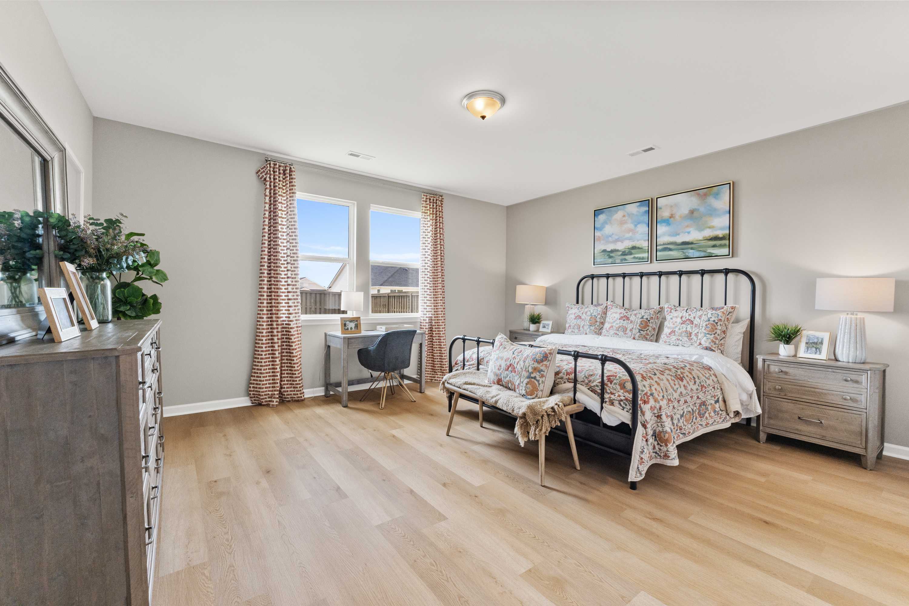 Spacious primary bedroom at The Meadows at Hampton Cove in Owens Cross Roads AL with hardwood floors, wrought iron bed, built-in desk