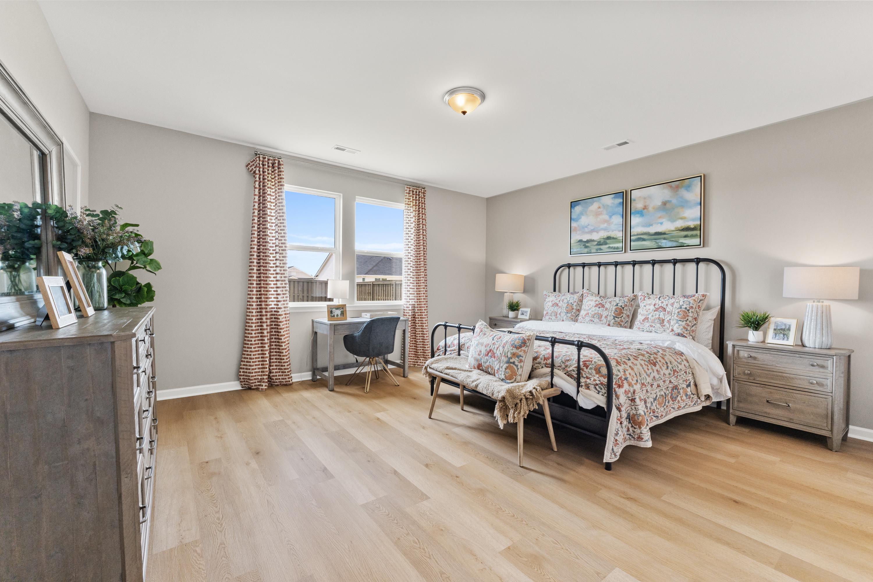 Spacious primary bedroom at The Meadows at Hampton Cove in Owens Cross Roads AL with hardwood floors, wrought iron bed, built-in desk