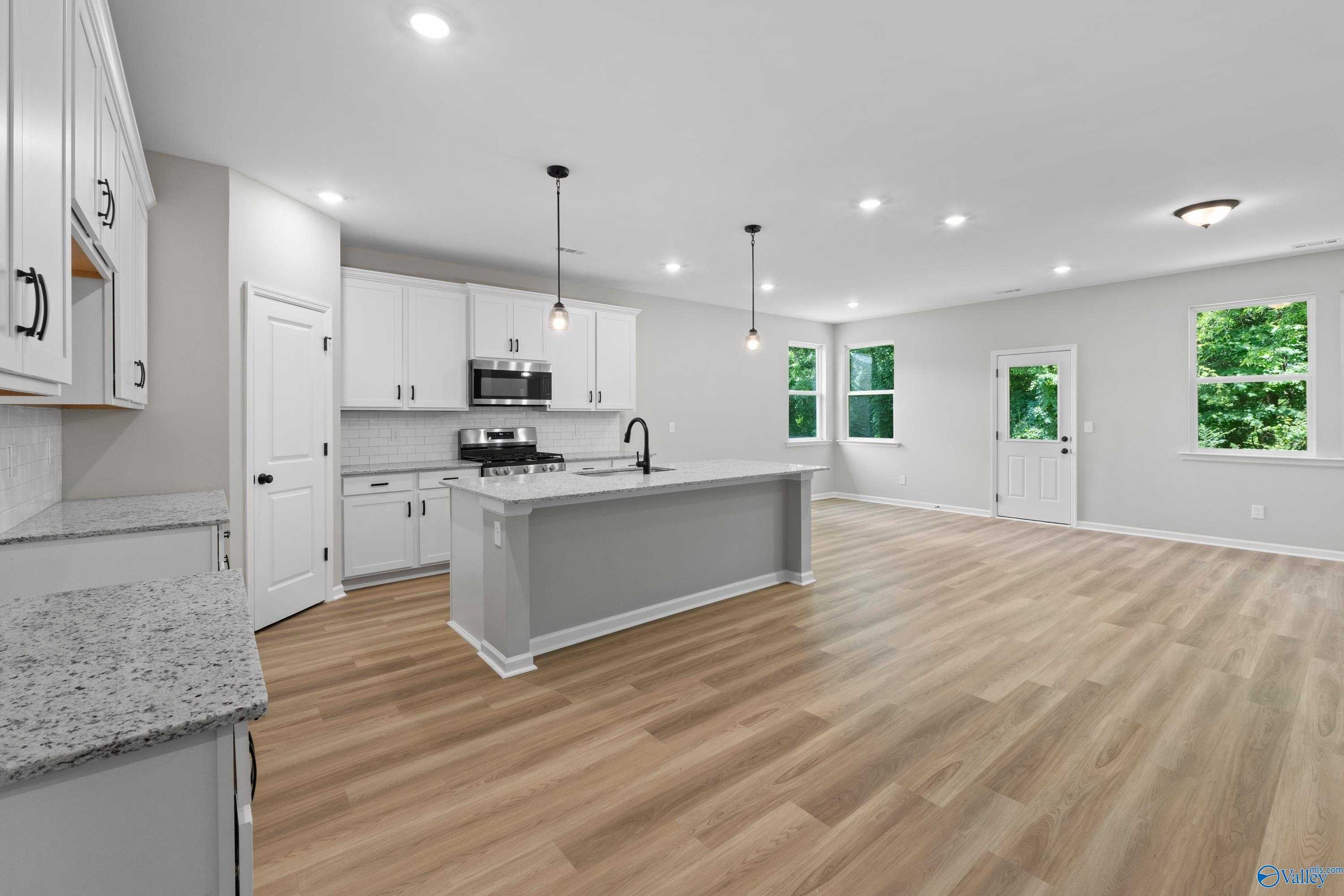 Modern open-concept kitchen featuring white cabinets, granite counters, stainless appliances, and island in Davidson Homes The Phoenix, Hazel Green, AL