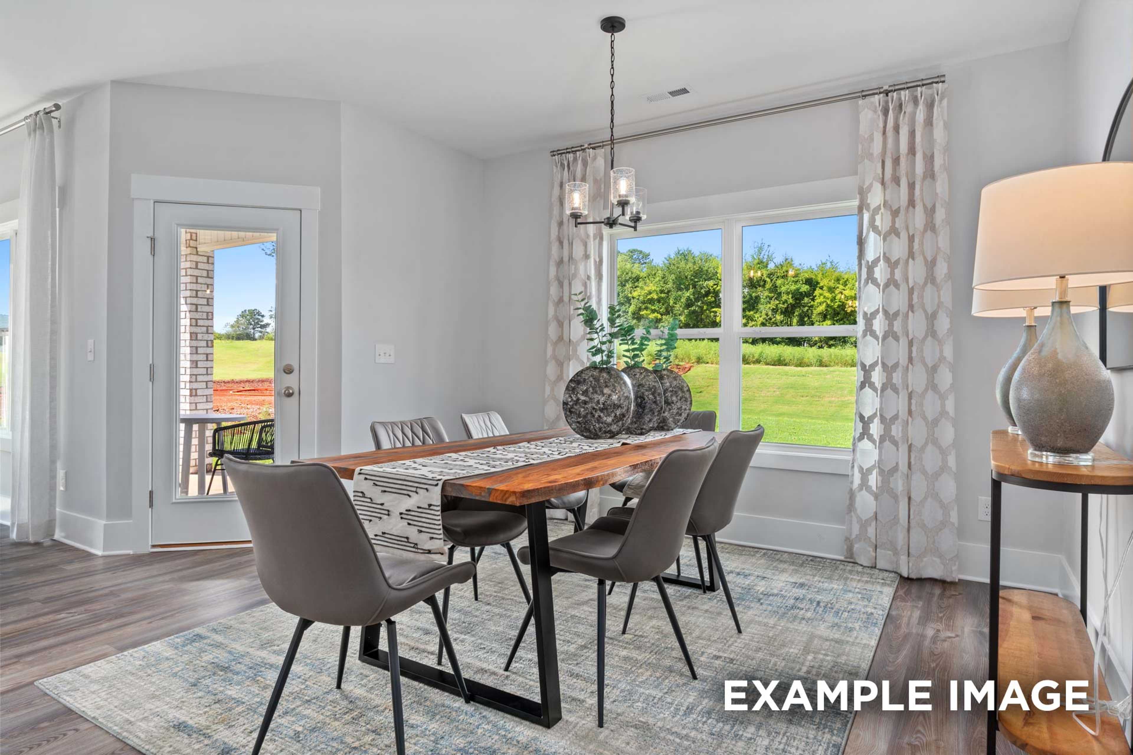 Spacious dining room in The Franklin C with wooden table, gray upholstered chairs, chandelier, and large windows overlooking green fields