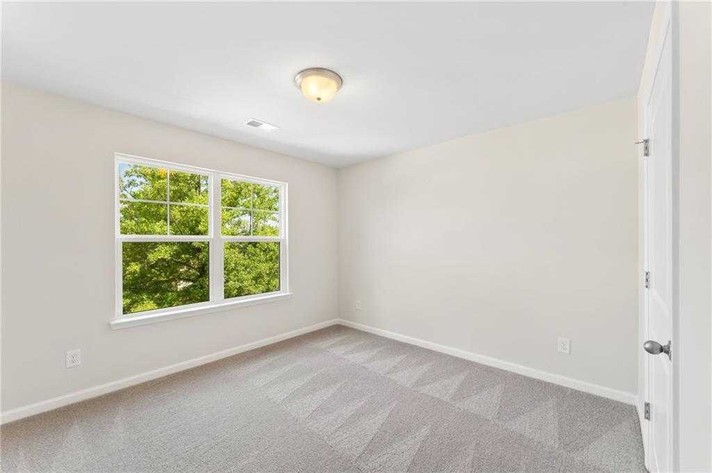 Bright secondary bedroom with large windows overlooking trees, beige walls, carpeted floor in Davidson Homes The Ash B, Dallas, Georgia