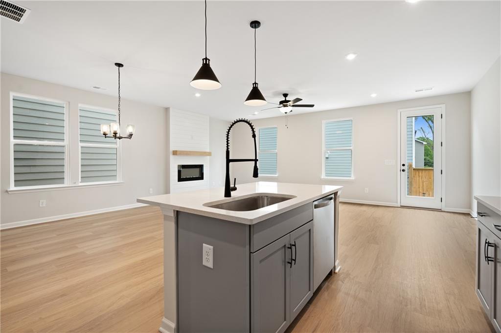 Modern open-concept kitchen with gray island, gooseneck faucet, pendant lights, and stone fireplace in The Marion A, Kennesaw, GA