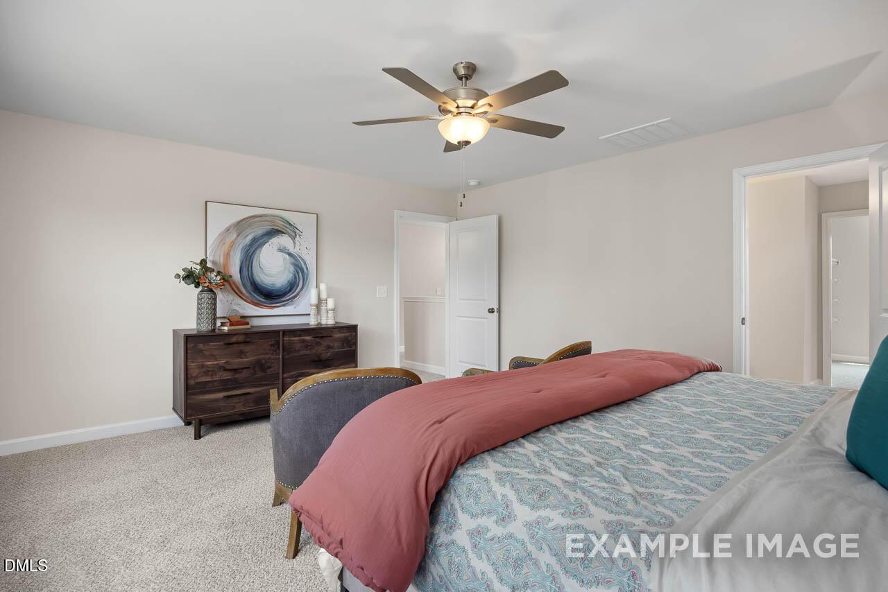 Elegant master bedroom with ceiling fan, abstract art, wooden dresser, and plush red duvet bed in Davidson Homes The Willow D, Lillington, NC