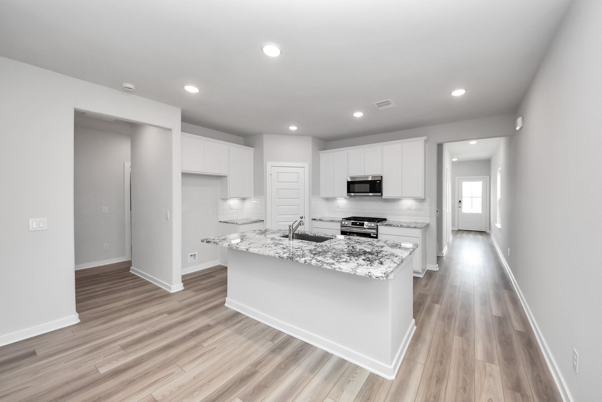 Modern kitchen with granite island, white cabinets, and stainless appliances in The Sabine E home, Windmill Estates, TX.