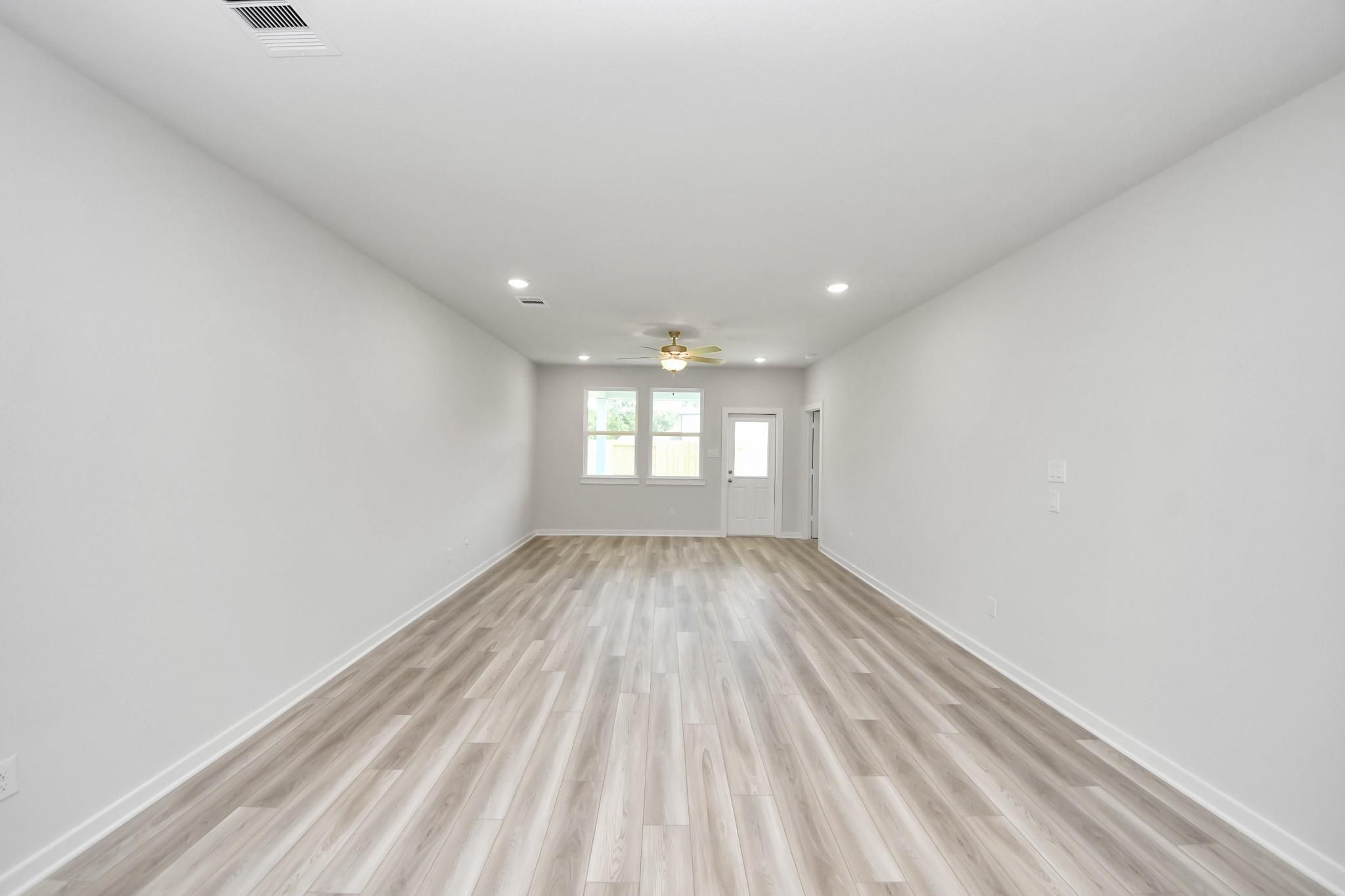 Spacious, light-filled living area with wood-look flooring in The Sabine F floor plan at Liberty Estates, Cleveland, Texas.