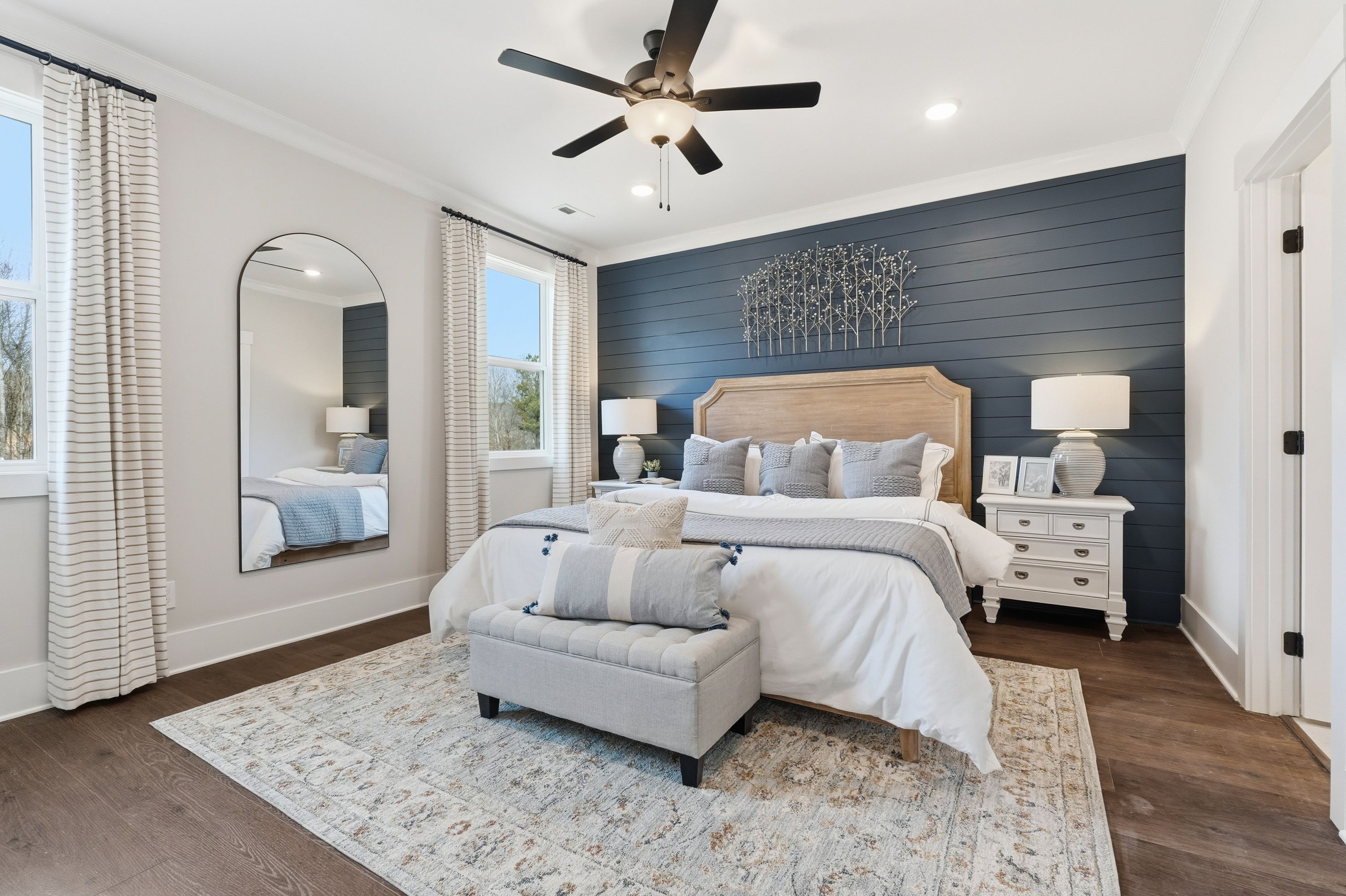 Spacious primary bedroom at Noble Ridge in Cullman AL with navy accent wall, king bed, arched mirror, ceiling fan, hardwood floors