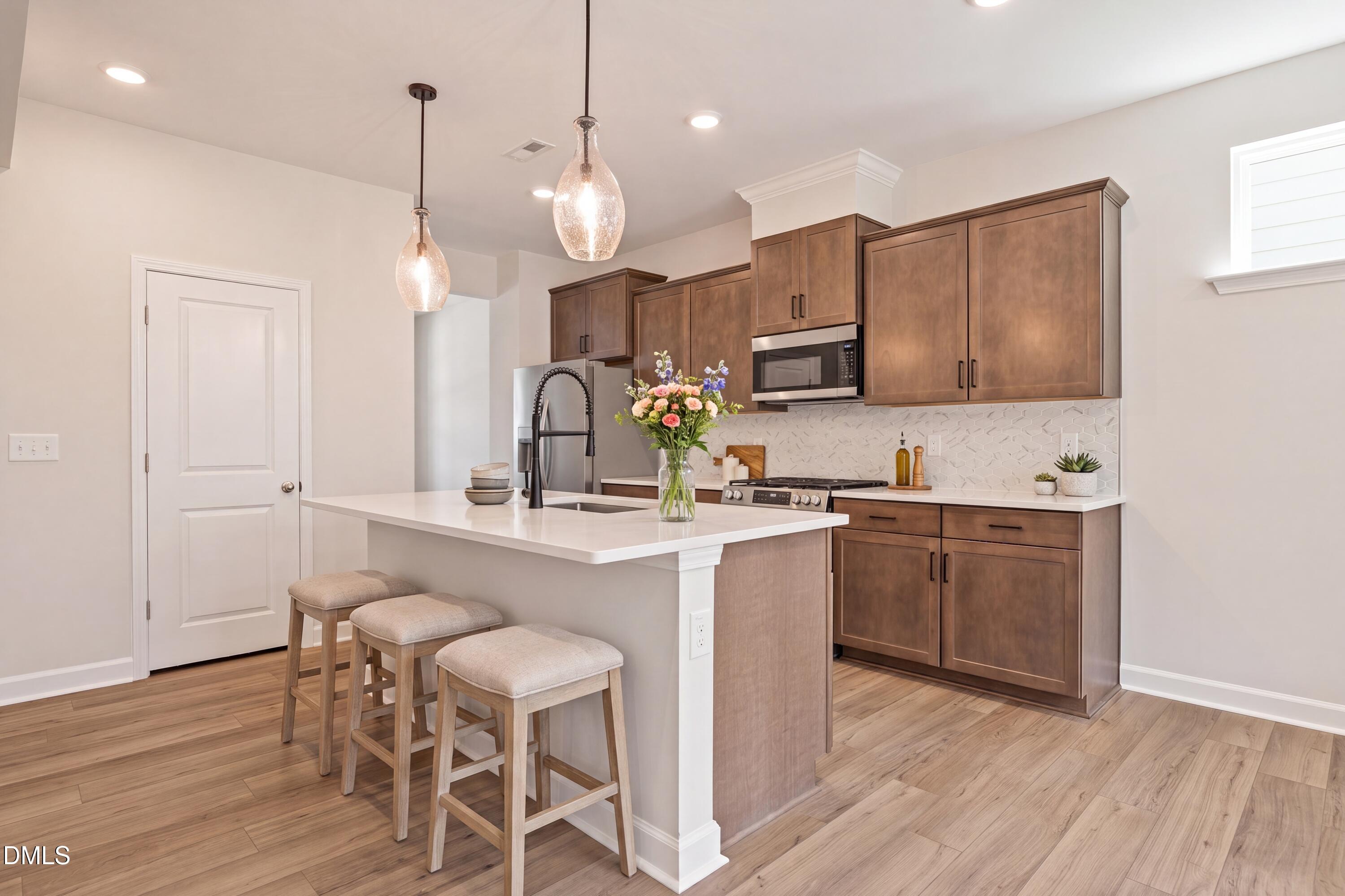 Modern kitchen with white island, wood cabinetry, and pendant lighting in The Willow D floor plan at Wendell Ridge, NC.
