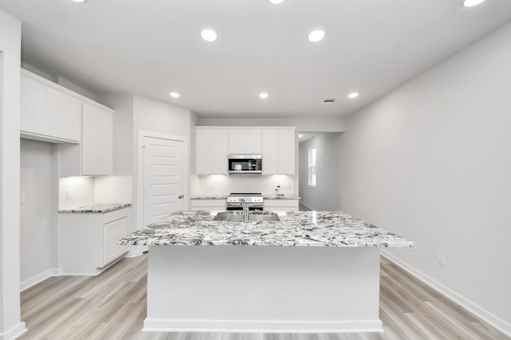 Modern kitchen with granite island and white cabinets in The Sabine F floor plan by Davidson Homes in Liberty Estates.