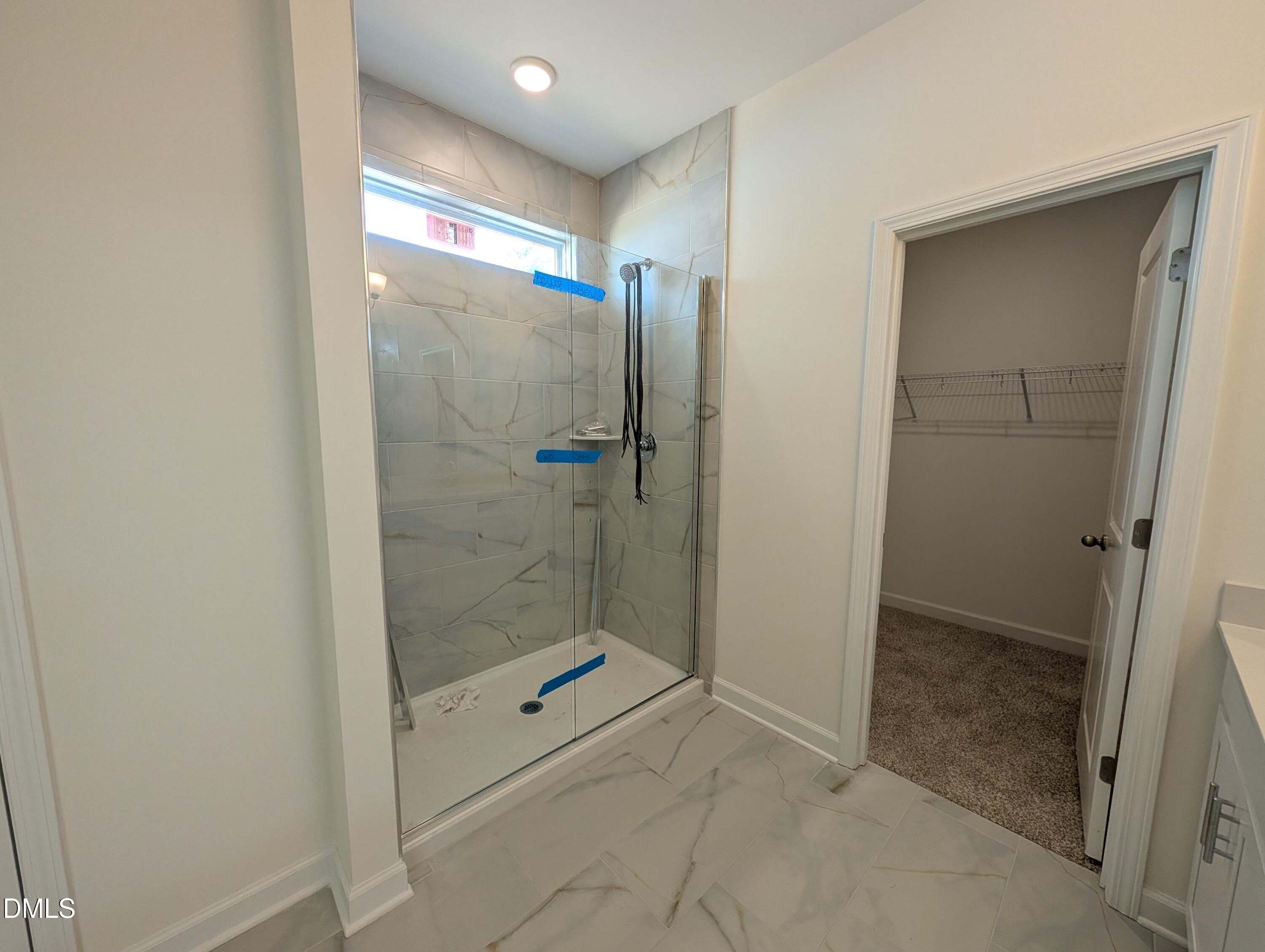 Glass walk-in shower with marble tile and walk-in closet in primary bath of Davidson Homes Magnolia A, Wendell, NC