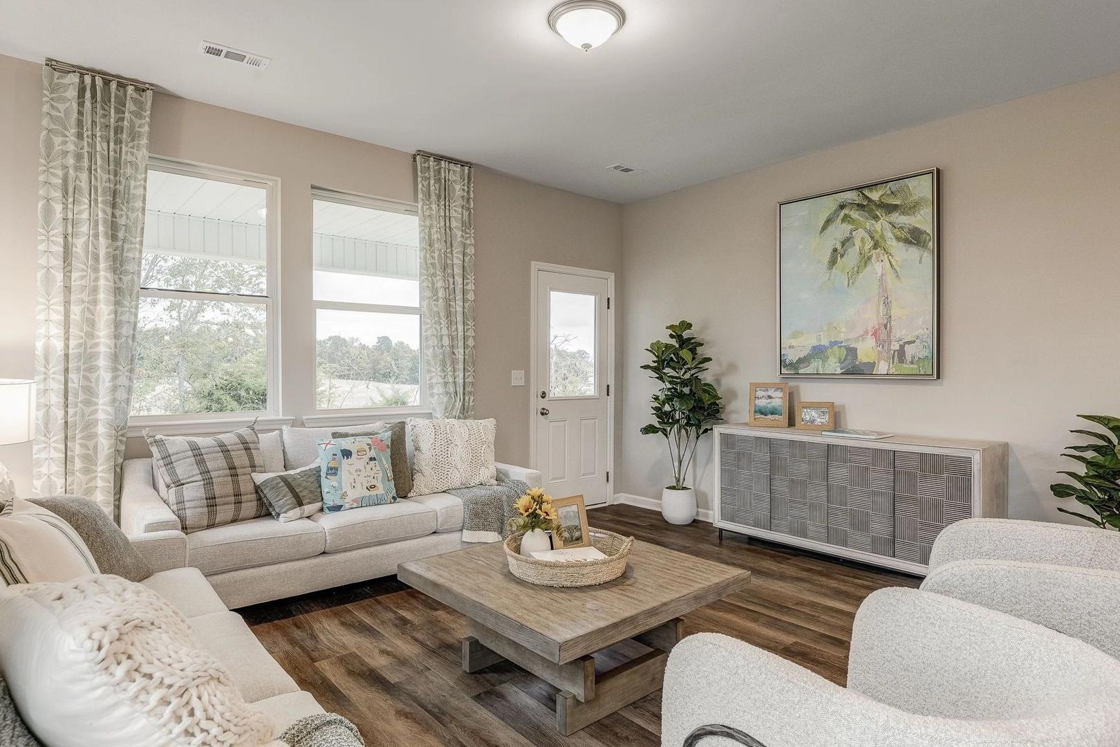 Spacious living room in Carroll Green, Harvest AL by Evermore Homes with beige walls, plush white sofa, hardwood floors, potted plants, and coastal palm art