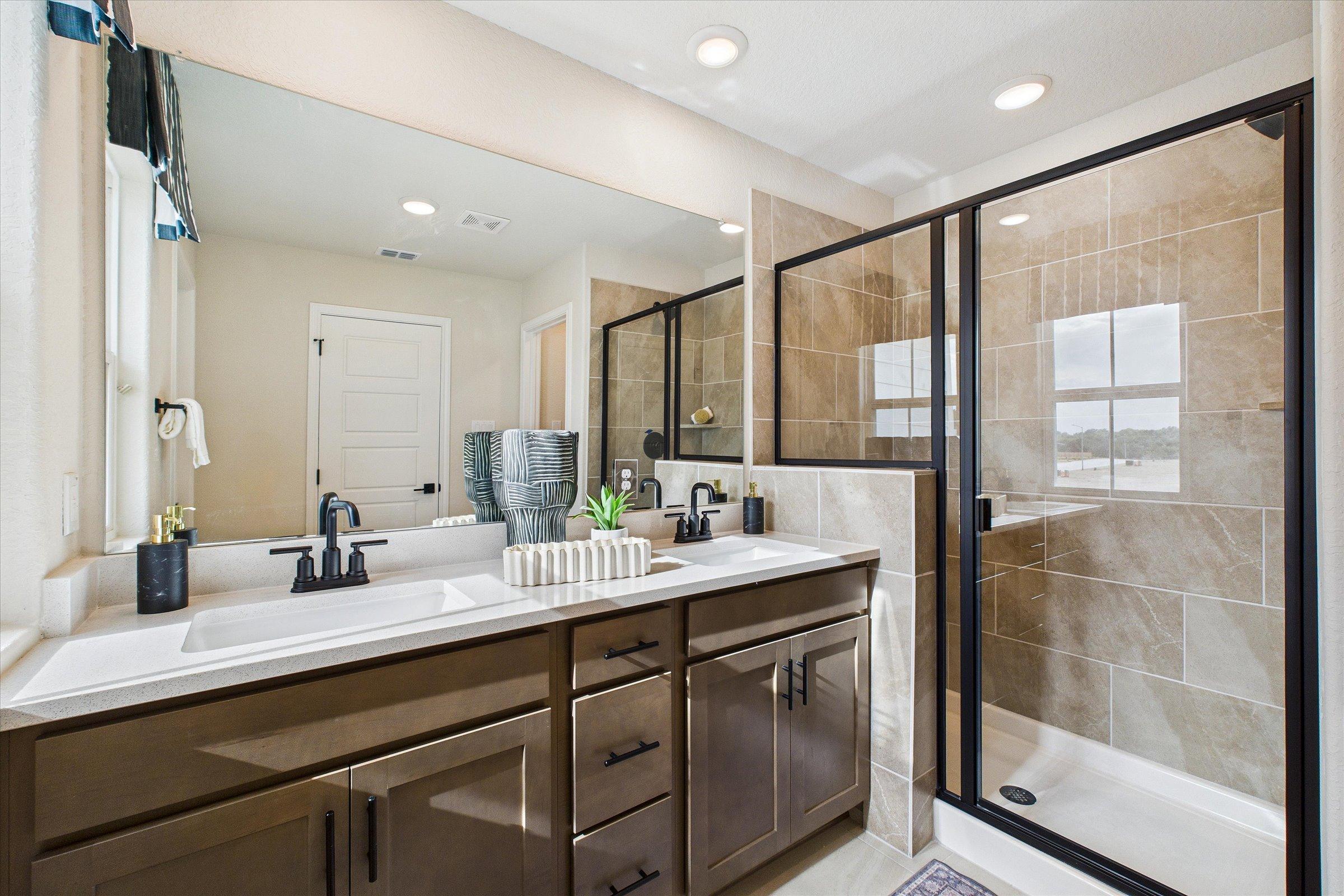 Spacious primary bathroom with double vanity, large mirror, and glass walk-in shower at Meadows at Oak Creek in San Antonio, Texas