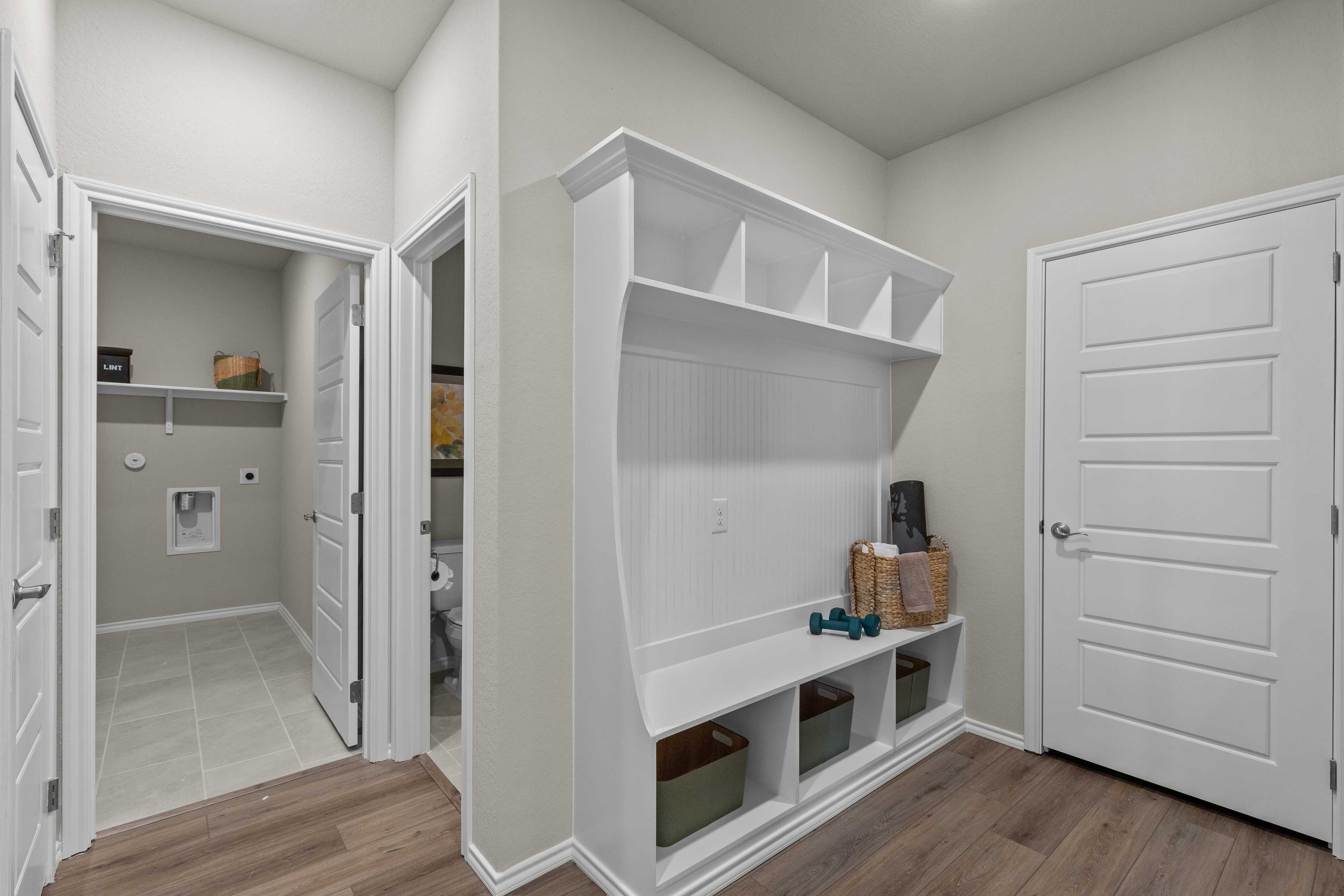 Spacious mudroom and laundry room in Comanche Ridge San Antonio TX home with white built-in cabinetry, shelves, cubbies and hardwood floors