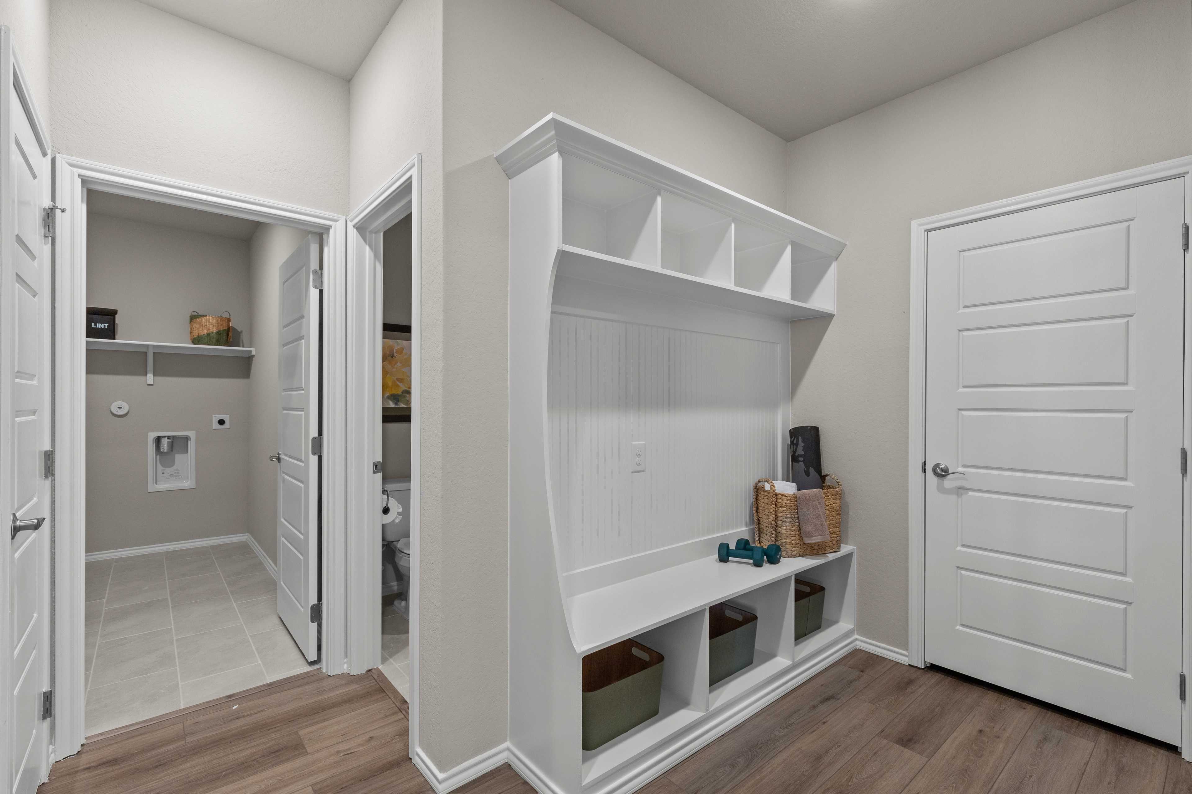 Spacious mudroom and laundry room in Comanche Ridge San Antonio TX home with white built-in cabinetry, shelves, cubbies and hardwood floors