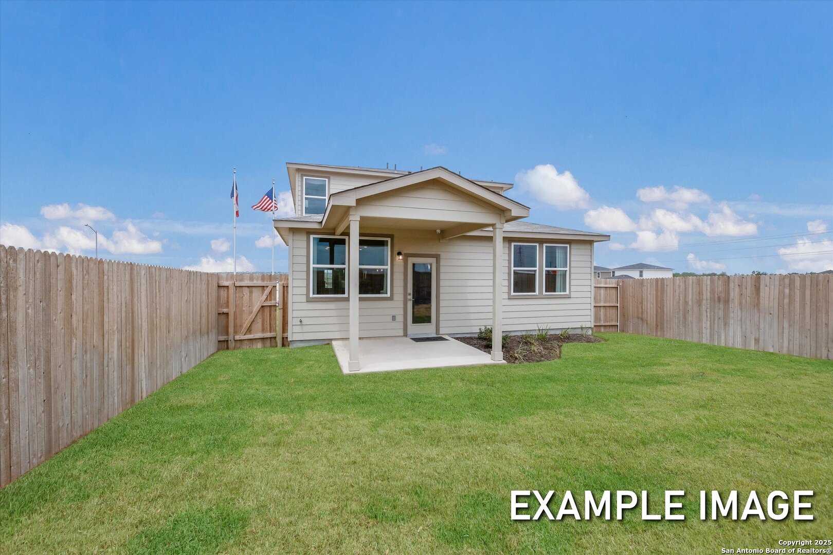Two-story beige home with covered porch, American flag, and wooden fence on lush green lawn in Davidson Homes The Brazos C, Agave San Antonio Texas