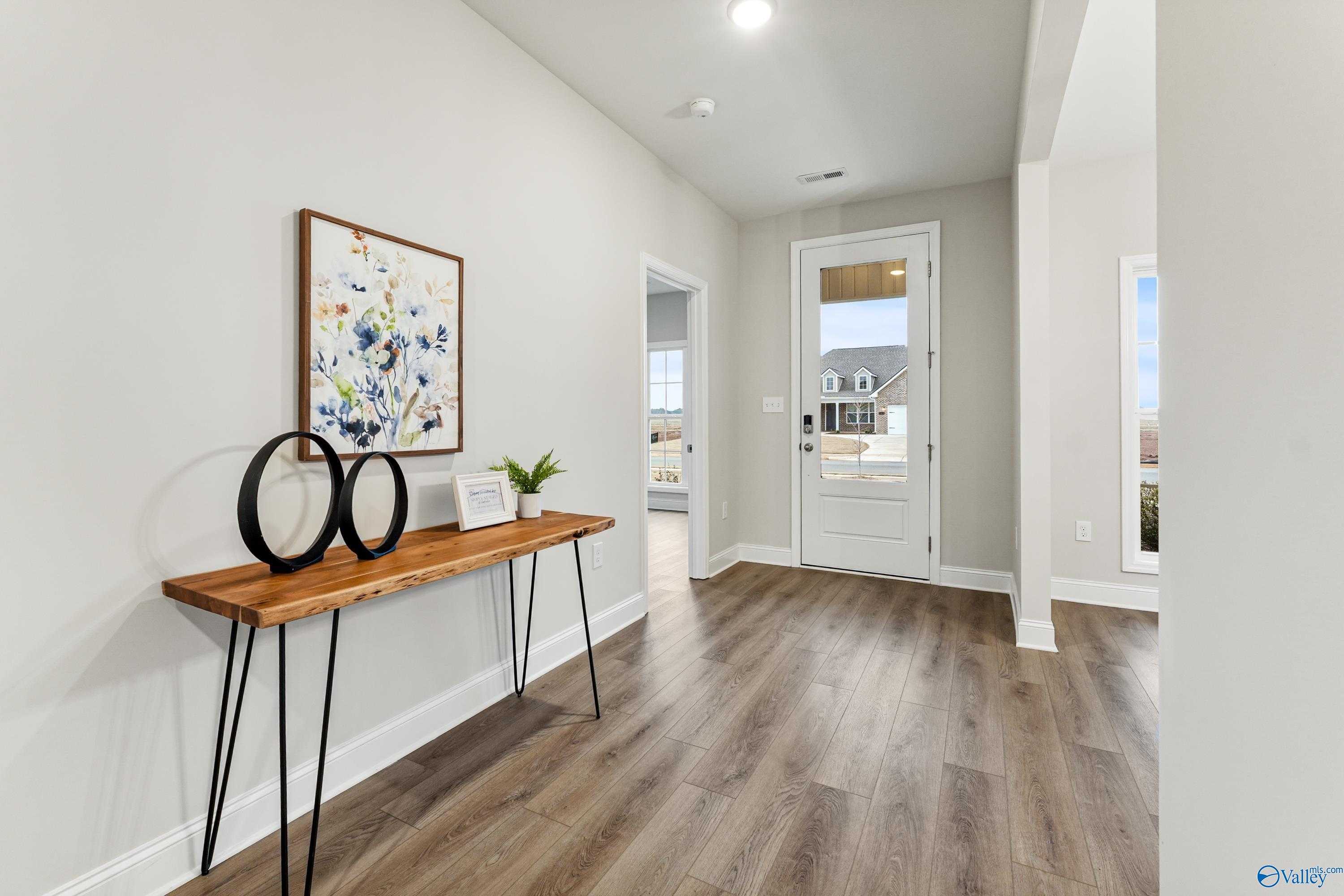 Elegant entryway hallway with wooden console table, abstract floral art, and light oak floors in The Finleigh home, Toney, Alabama