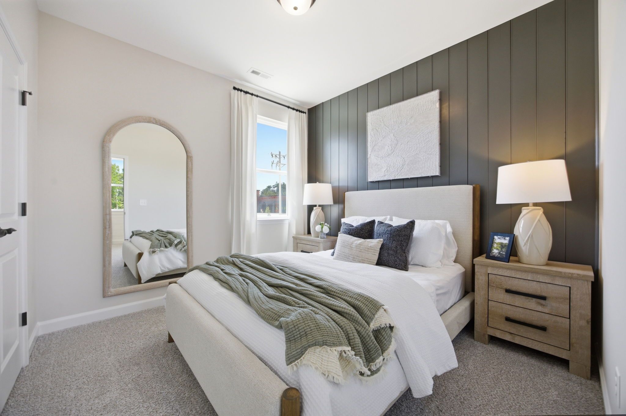 Spacious bedroom at Forestville Yard in Knightdale NC with king bed, gray shiplap accent wall, arched mirror, and bedside lamps