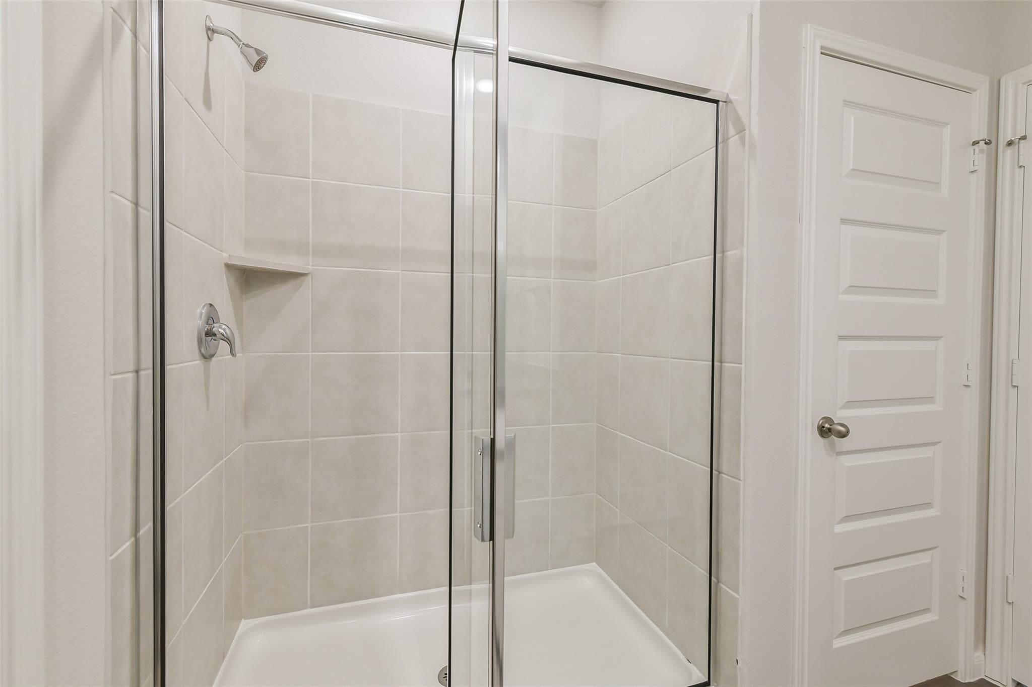 Modern walk-in shower with frameless glass enclosure, beige subway tiles, and built-in shelf in Davidson Homes The Brazos F, Conroe, Texas