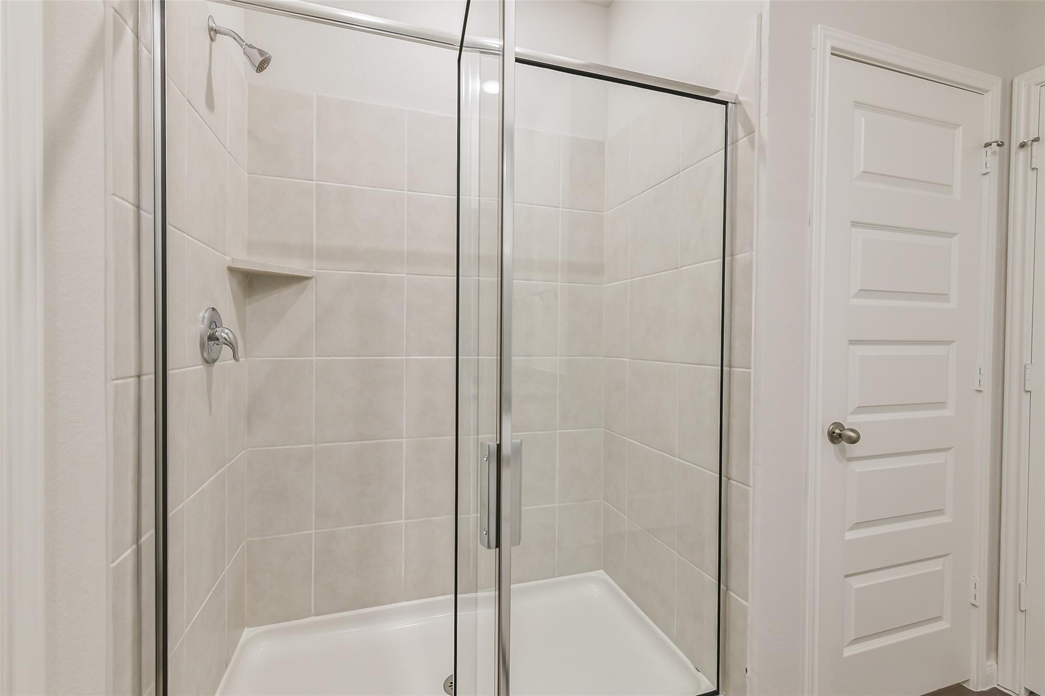 Modern walk-in shower with glass door and beige subway tiles in Davidson Homes The Brazos F, Conroe, Texas