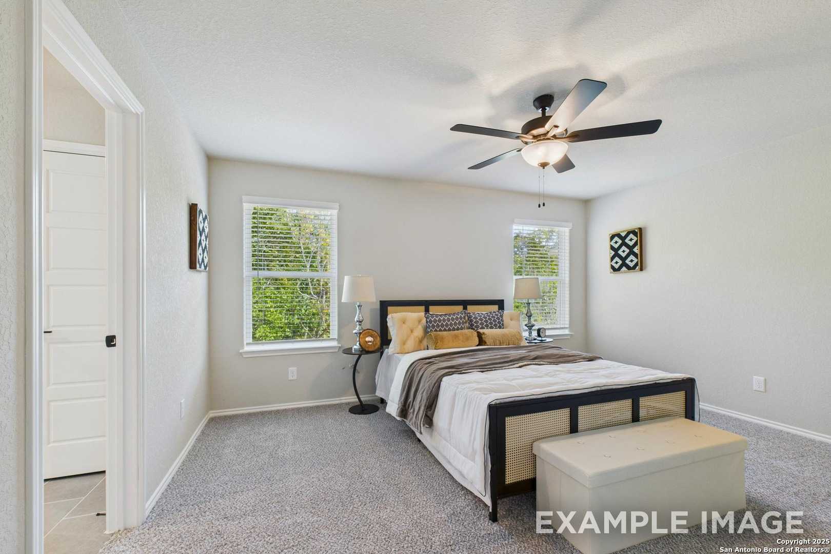 Spacious master bedroom with king bed, ceiling fan, and large windows in Davidson Homes The Charlotte A, San Antonio