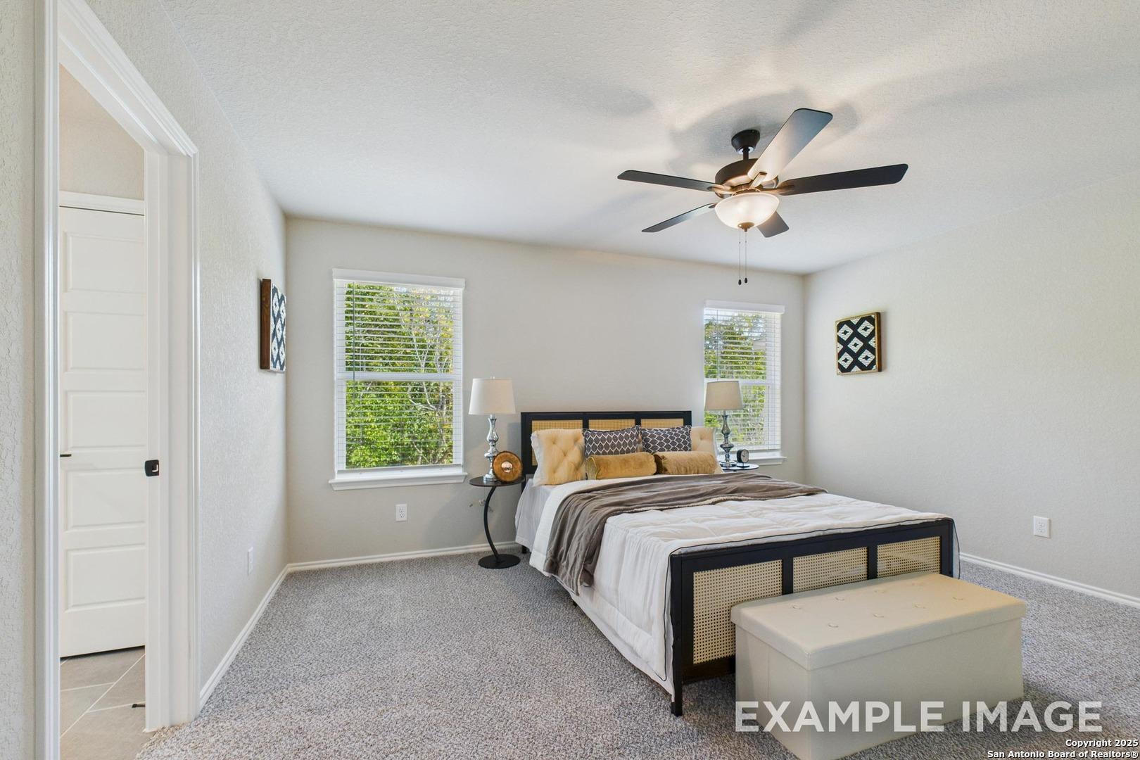 Serene master bedroom with plush king bed, ceiling fan, and tree-view windows in Davidson Homes Charlotte B, San Antonio