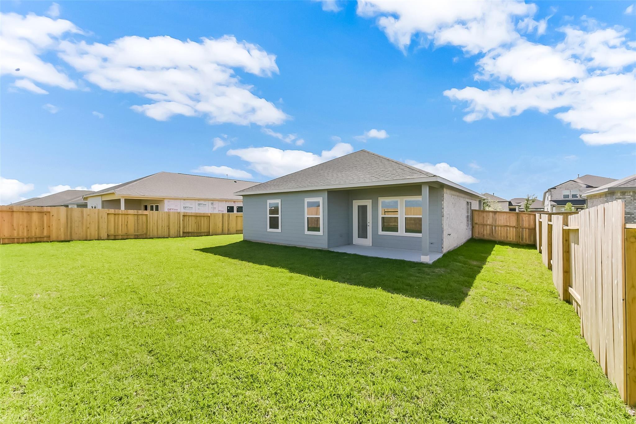 Gray single-story home with white-trimmed windows, lush green lawn, wooden fence, under blue sky in River Ranch Meadows, Dayton, Texas