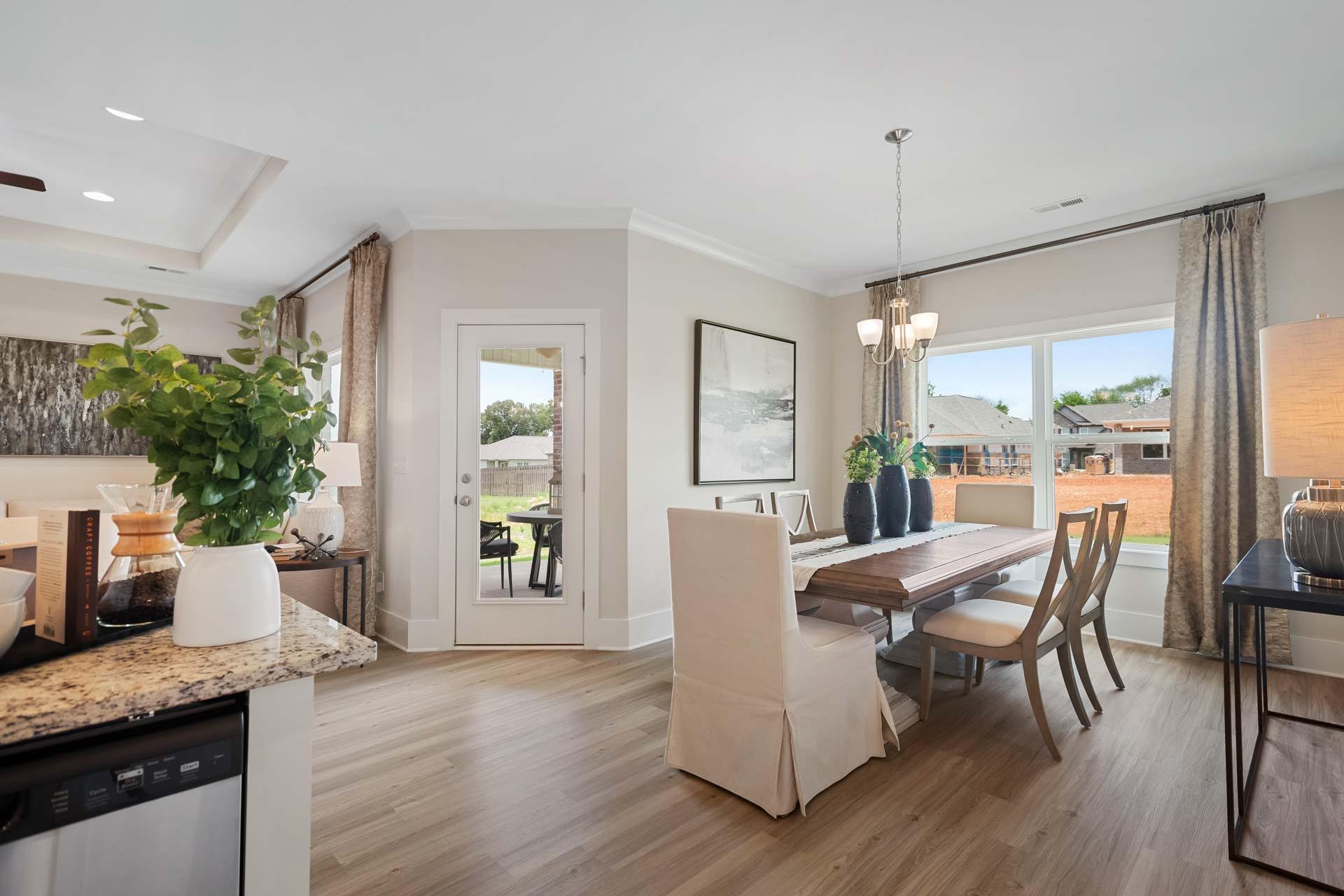 Spacious dining room at Flint Meadows in New Market AL with wooden table, neutral chairs, hardwood floors, and large windows to patio