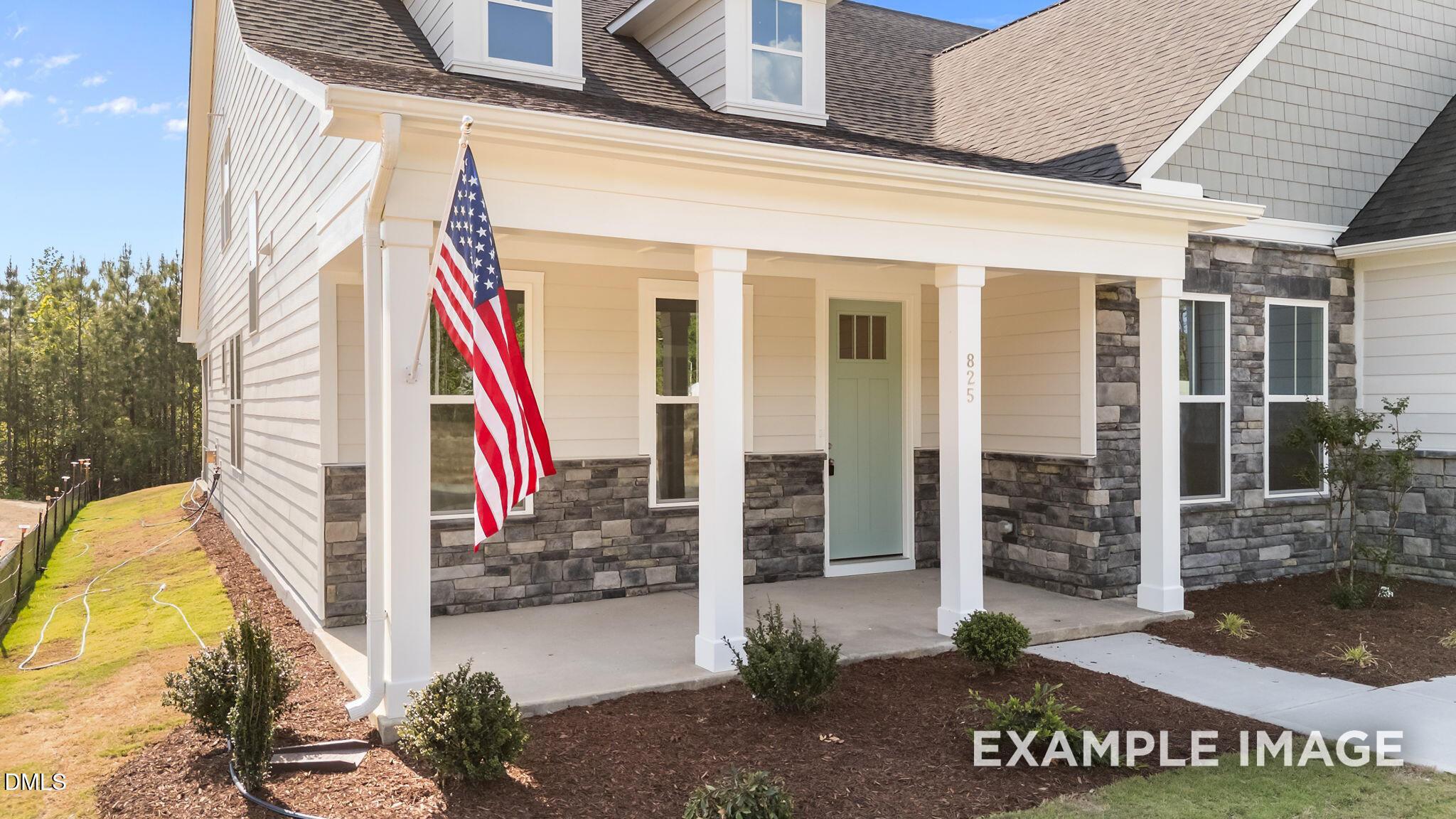 Charming covered front porch with stone accents and American flag on The Magnolia B home in Retreat at North Main.