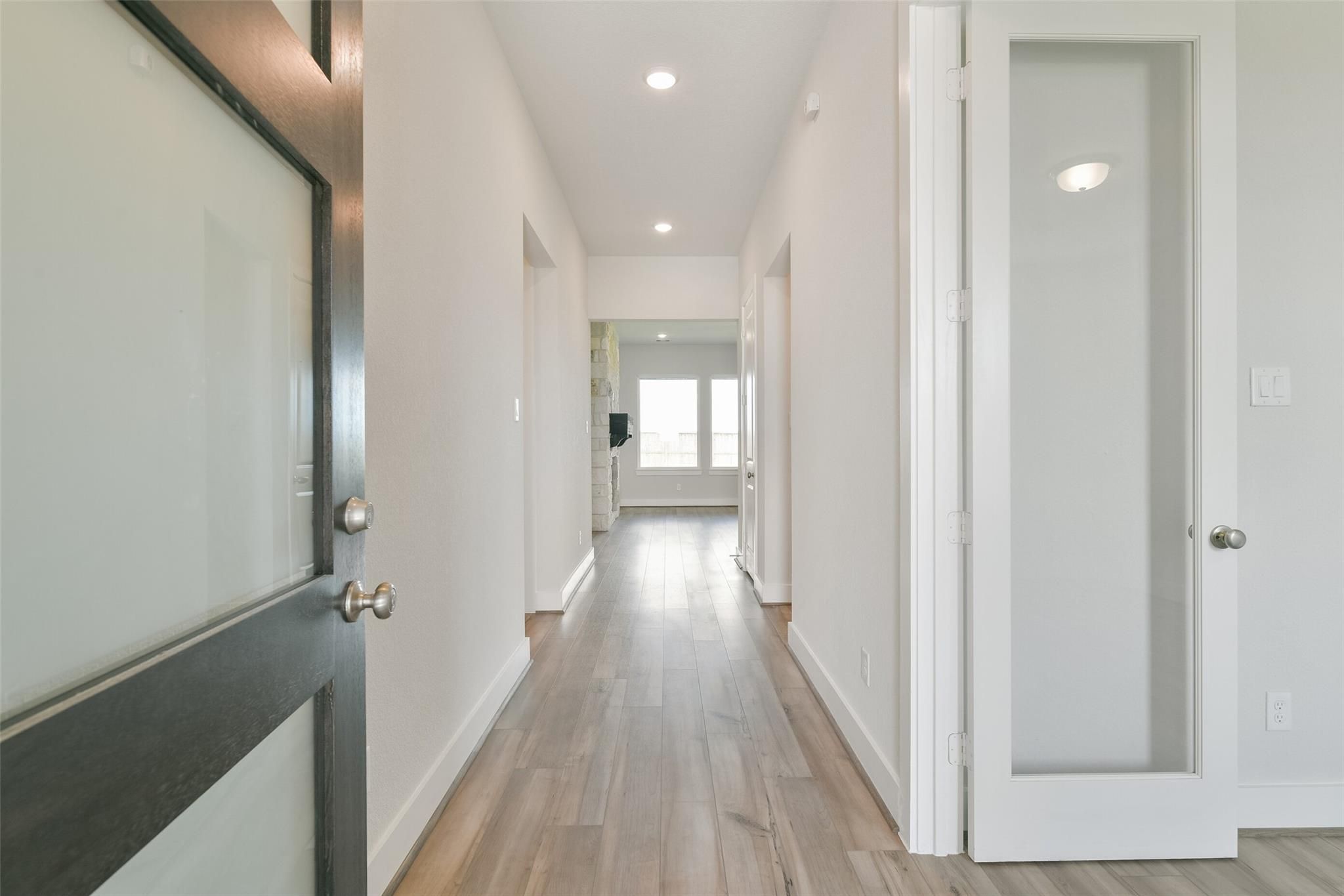 Bright hallway with light wood floors, frosted glass doors, and recessed lighting in Davidson Homes The Edward A, Lago Mar, Texas City