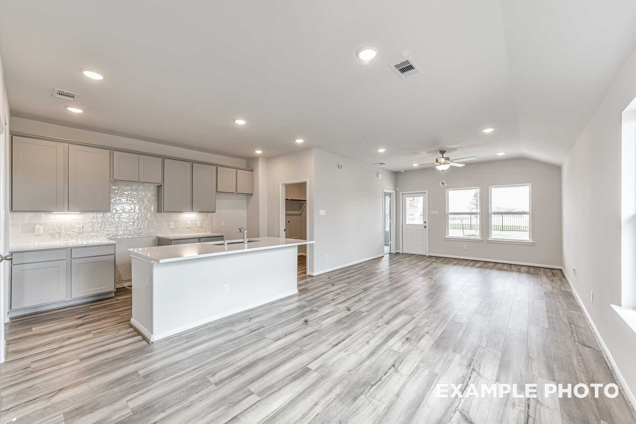 Open-concept kitchen and living area in The Costa C featuring gray cabinets, white island, subway tile backsplash, and wood-look flooring