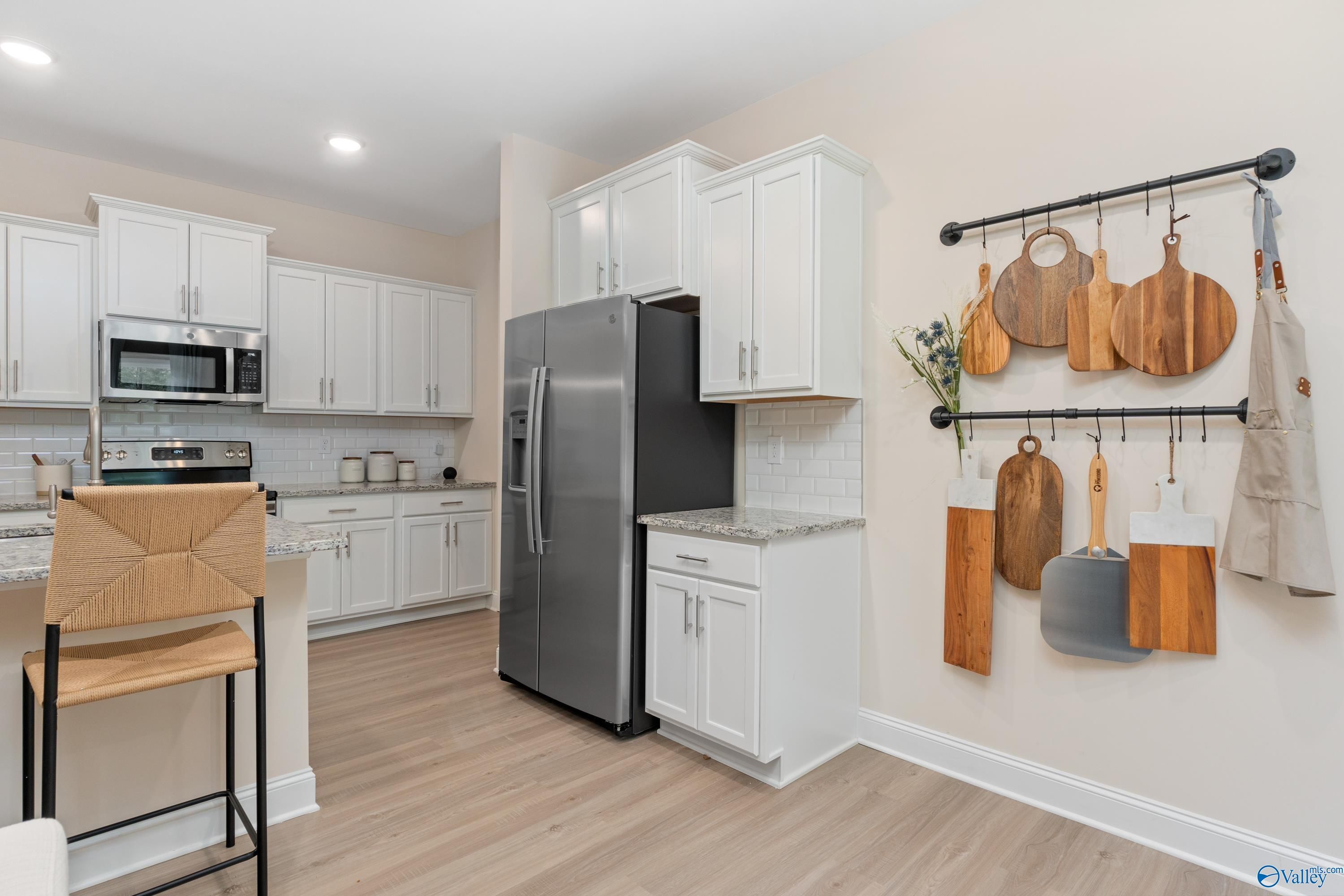 Modern kitchen with white shaker cabinets, stainless steel fridge, subway tile backsplash, and hanging wooden utensils in Davidson Homes The Camden, Huntsville, Alabama