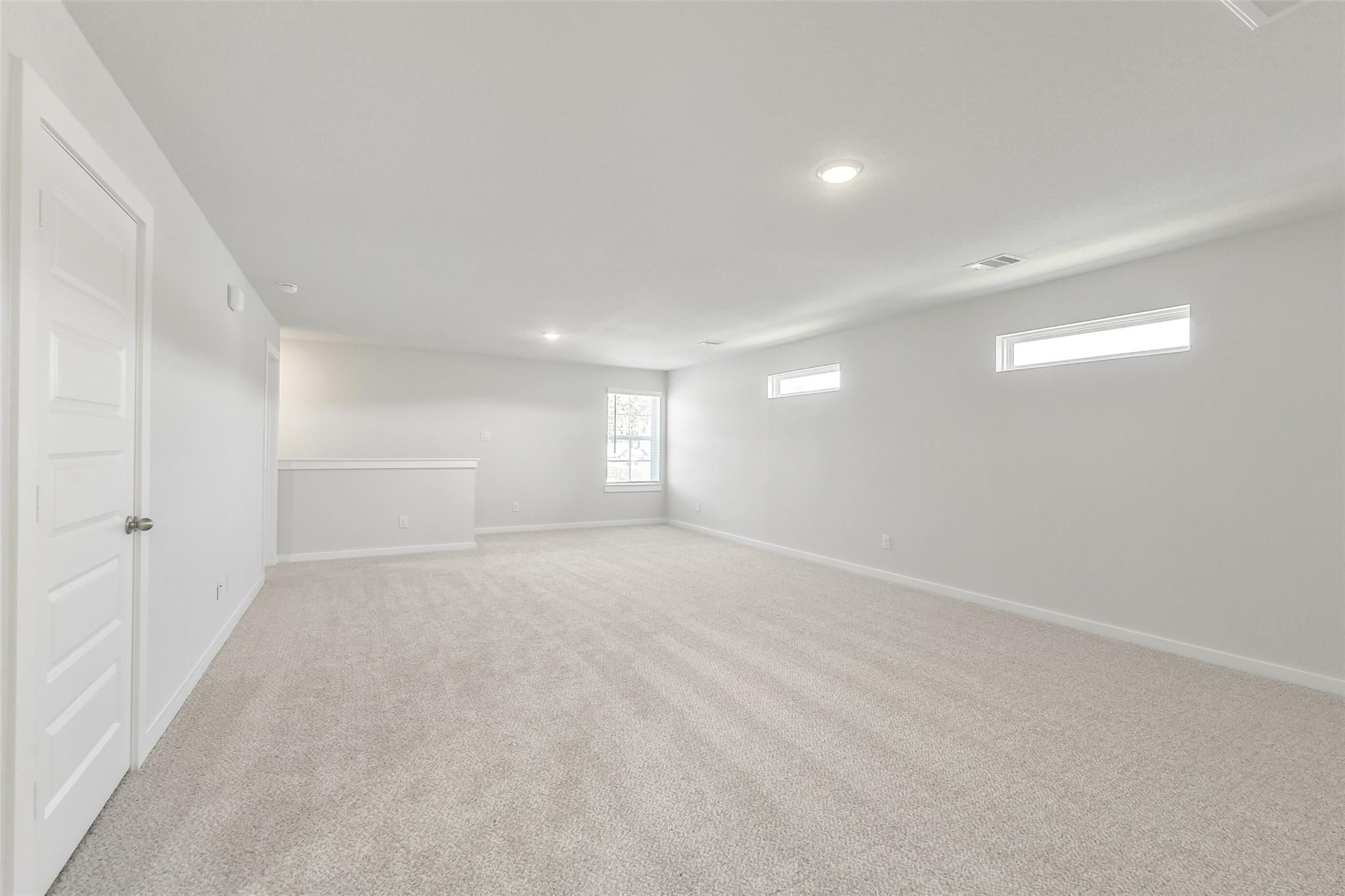 Spacious upstairs loft with vaulted ceiling, beige carpet, white walls, and windows in Davidson Homes The San Marcos E, Cleveland, Texas