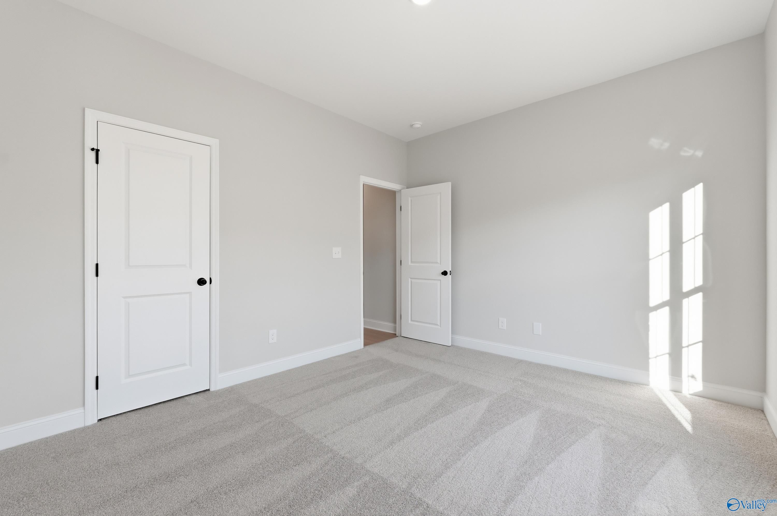 Bright empty bedroom with gray carpet, white doors, and natural light in Davidson Homes The Daphne C, Athens, Alabama