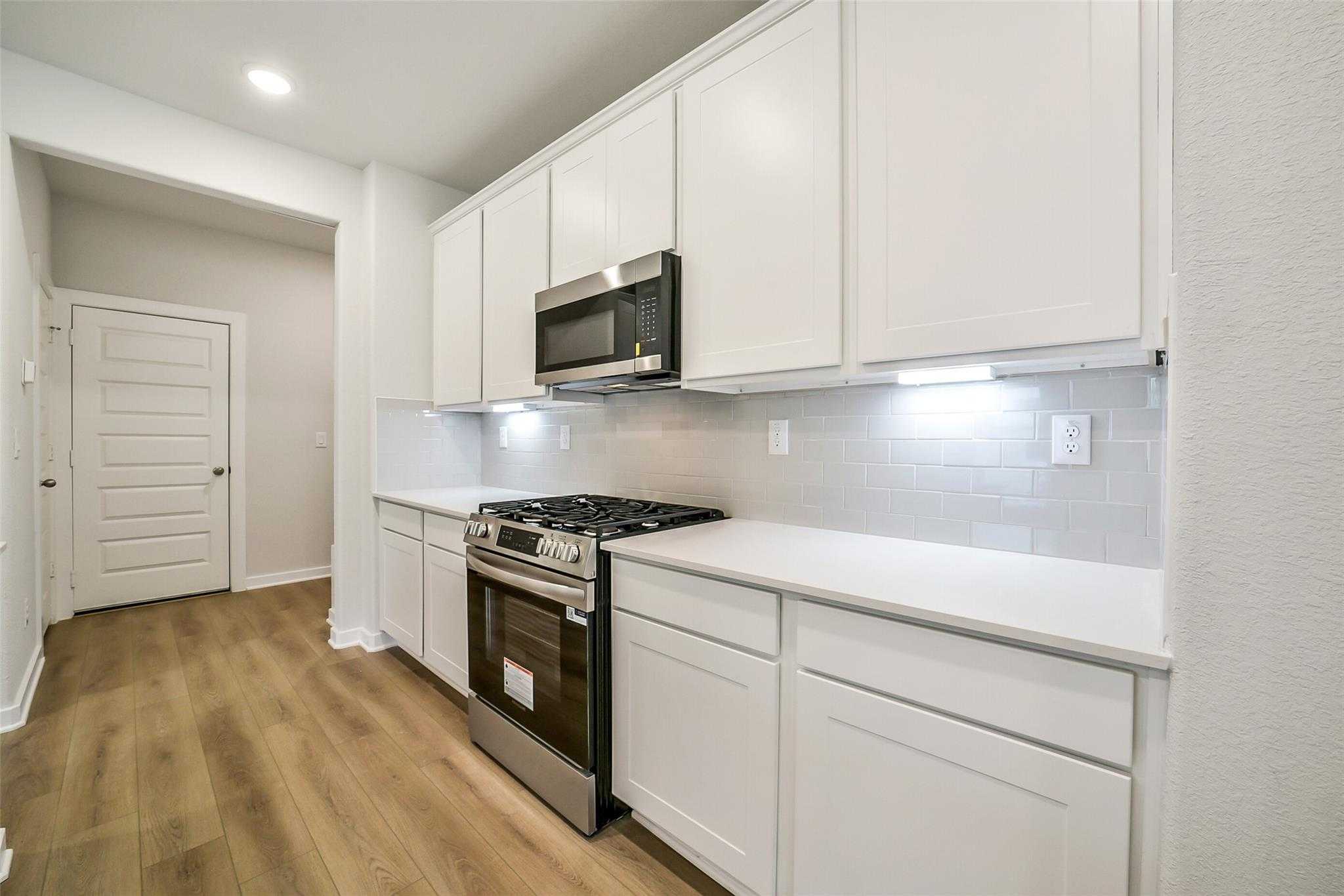 Modern white kitchen with stainless appliances, quartz counters, subway tile backsplash in Davidson Homes The Blanco E, Magnolia TX