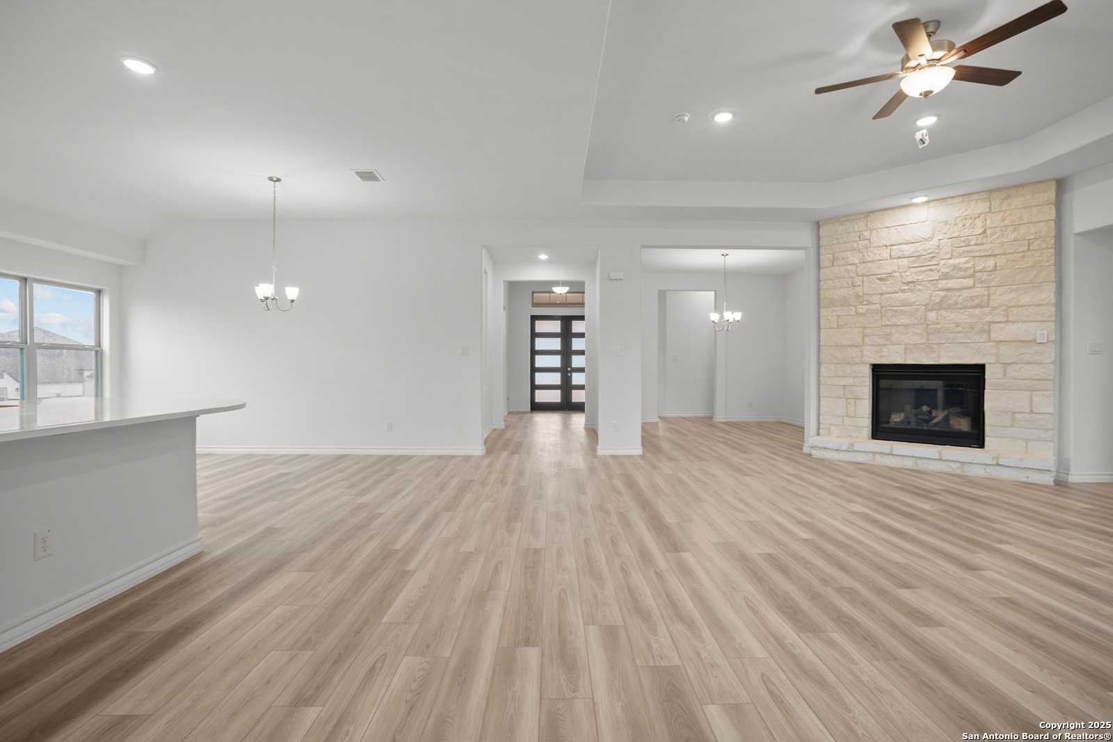 Open-concept great room with stone gas fireplace, luxury vinyl plank floors, and high ceilings in Davidson Homes Summerlin B, Castroville, TX