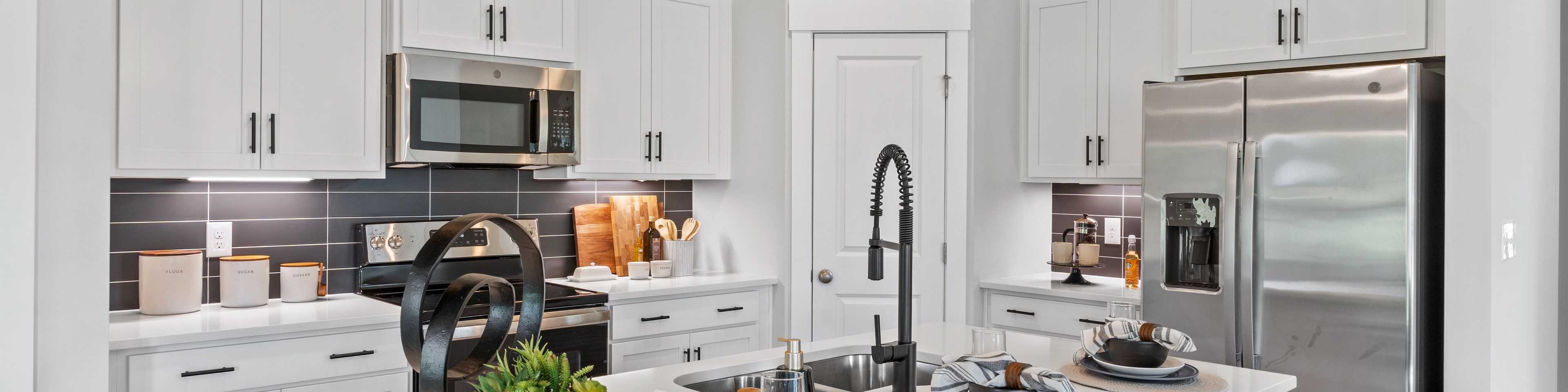 Modern white kitchen in Blue Spring Huntsville AL by Davidson Homes with quartz island black stools stainless appliances