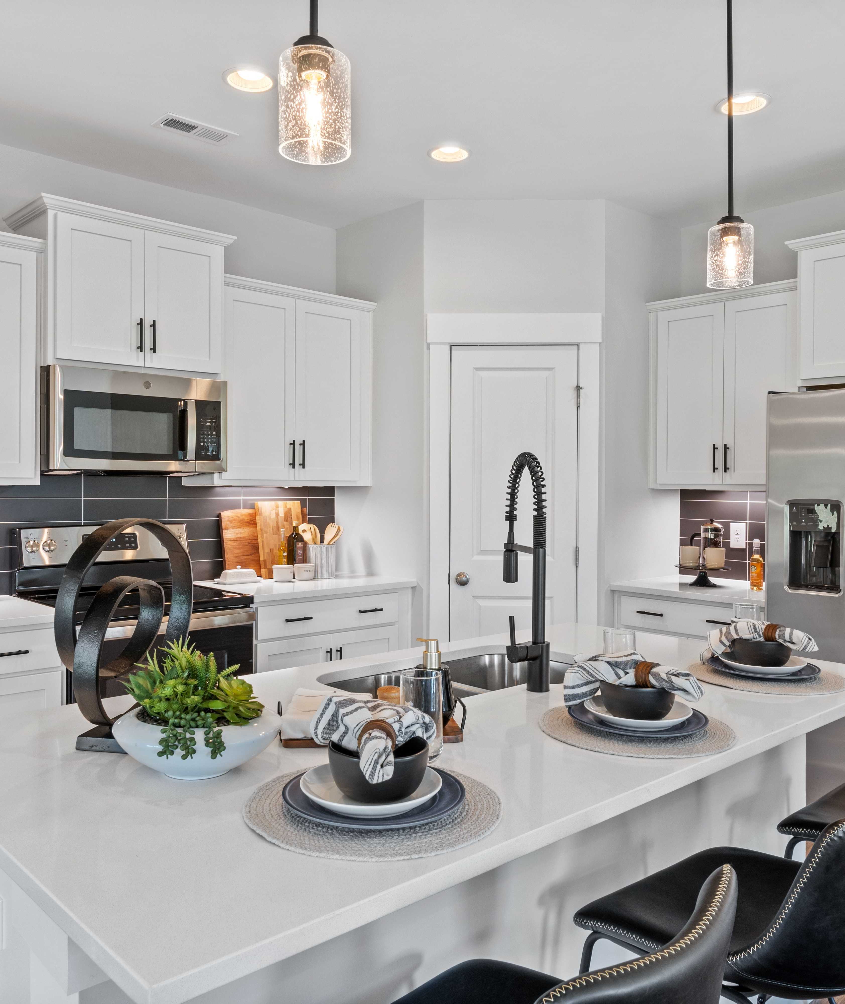 Modern white kitchen in Blue Spring Huntsville AL by Davidson Homes with quartz island black stools stainless appliances