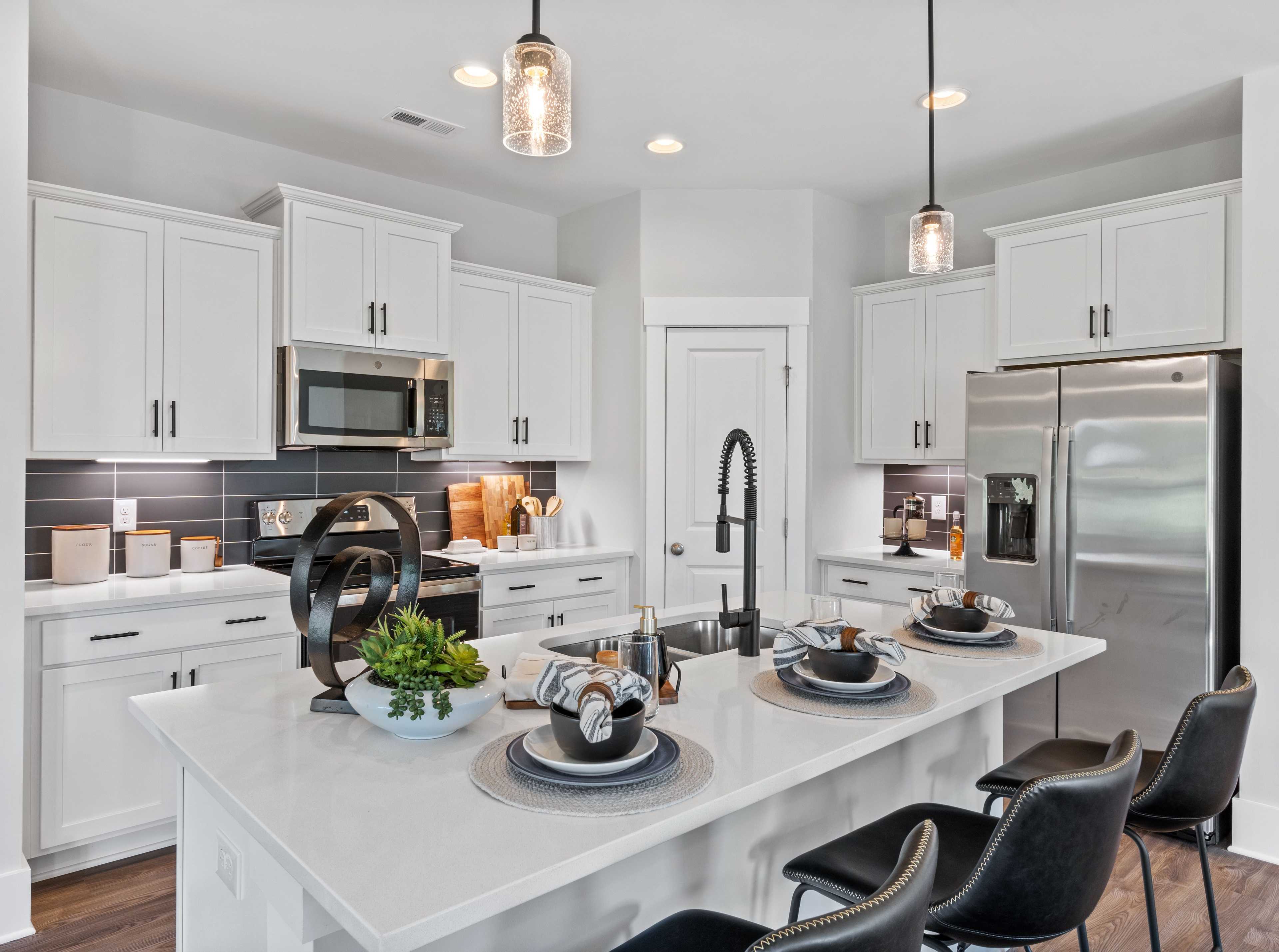 Modern white kitchen in Blue Spring Huntsville AL by Davidson Homes with quartz island black stools stainless appliances