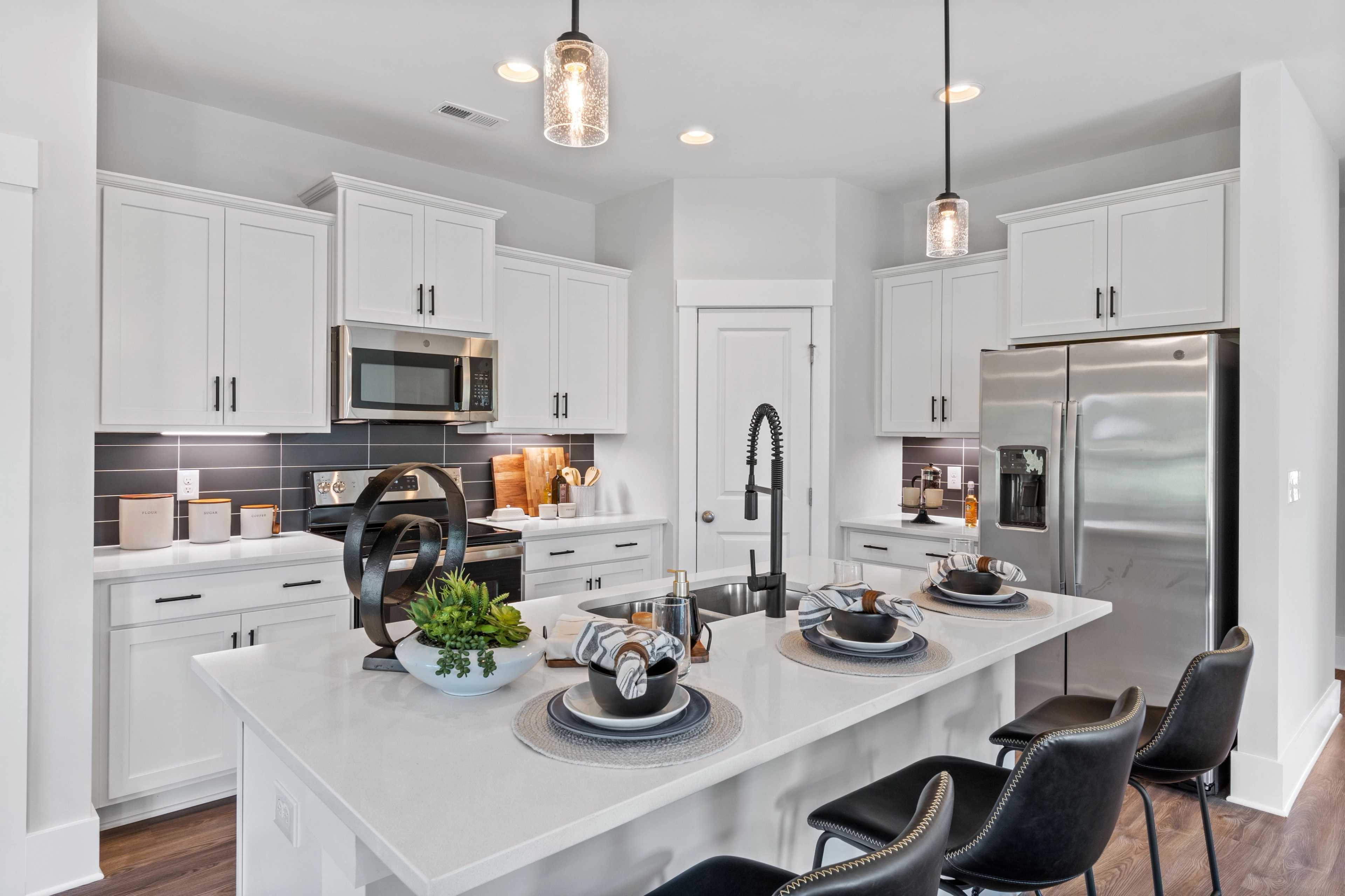Modern white kitchen in Blue Spring Huntsville AL by Davidson Homes with quartz island black stools stainless appliances