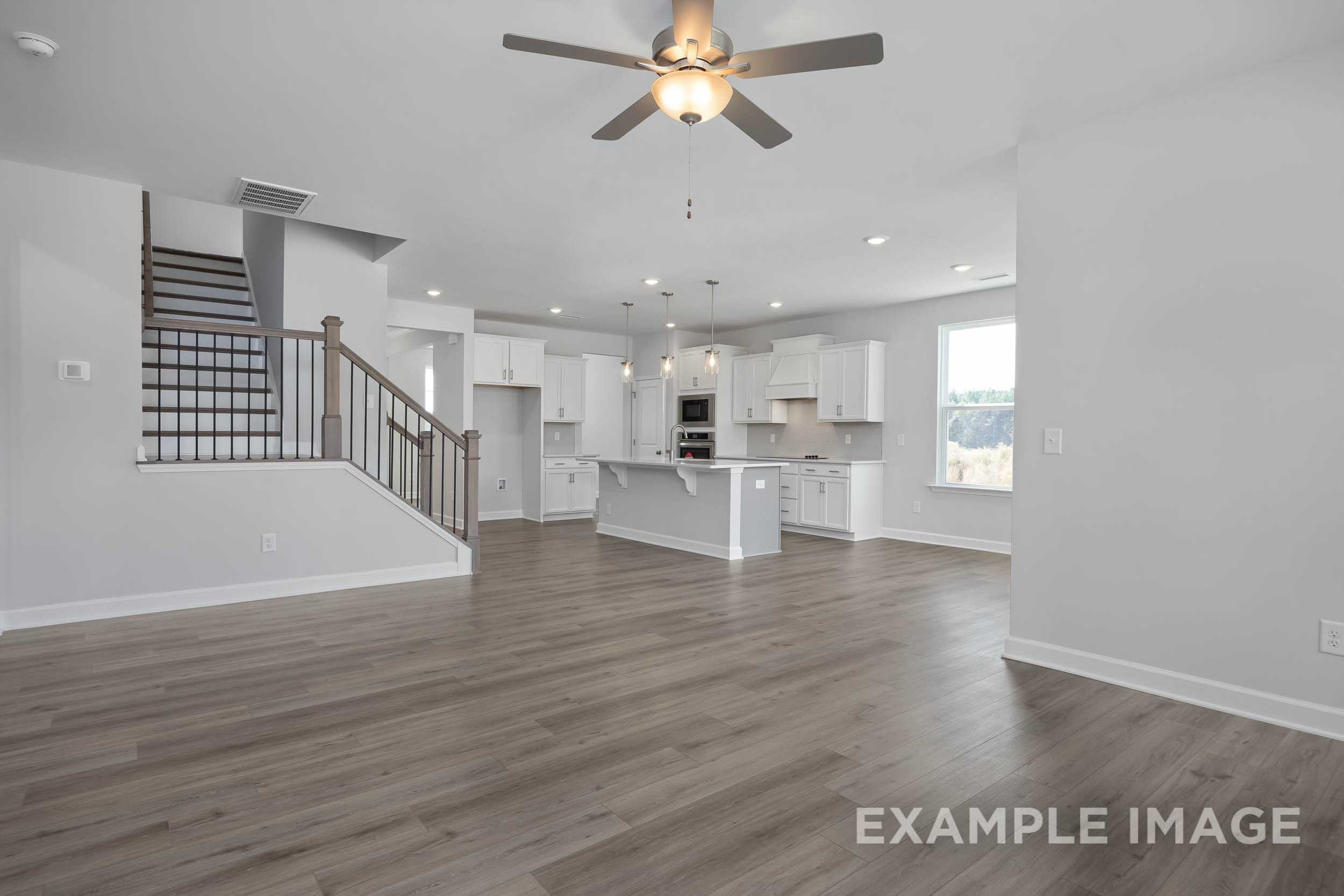 Spacious open-concept kitchen in The Ash home with white cabinets, large island, hardwood floors, and ceiling fan